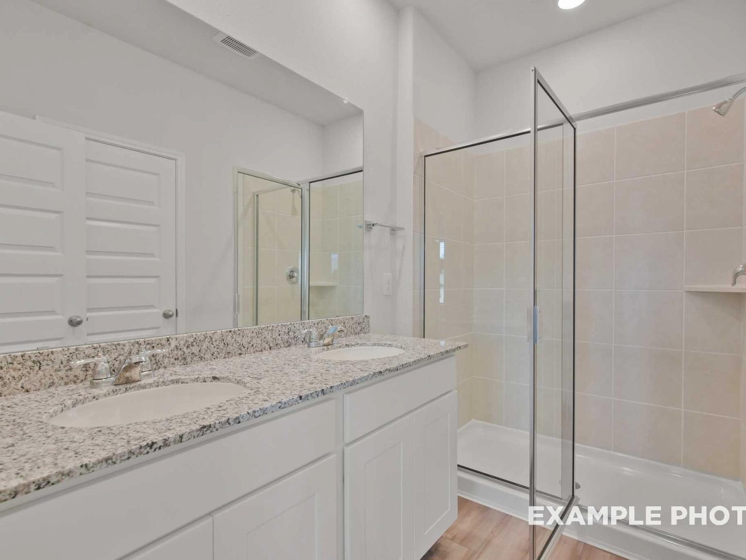 Modern master bathroom featuring double granite vanity, frameless glass shower, and white cabinets in Davidson Homes The Comal F, Conroe, Texas