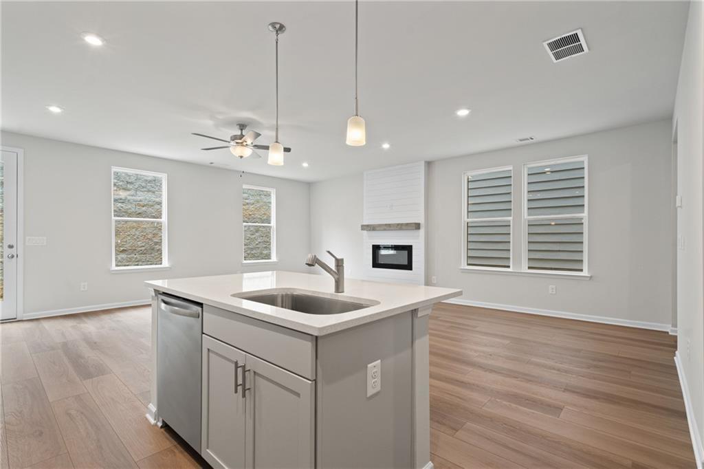 Modern open-concept kitchen with island sink, pendant lights, ceiling fan, and gas fireplace in The Marion B home, Kennesaw, GA
