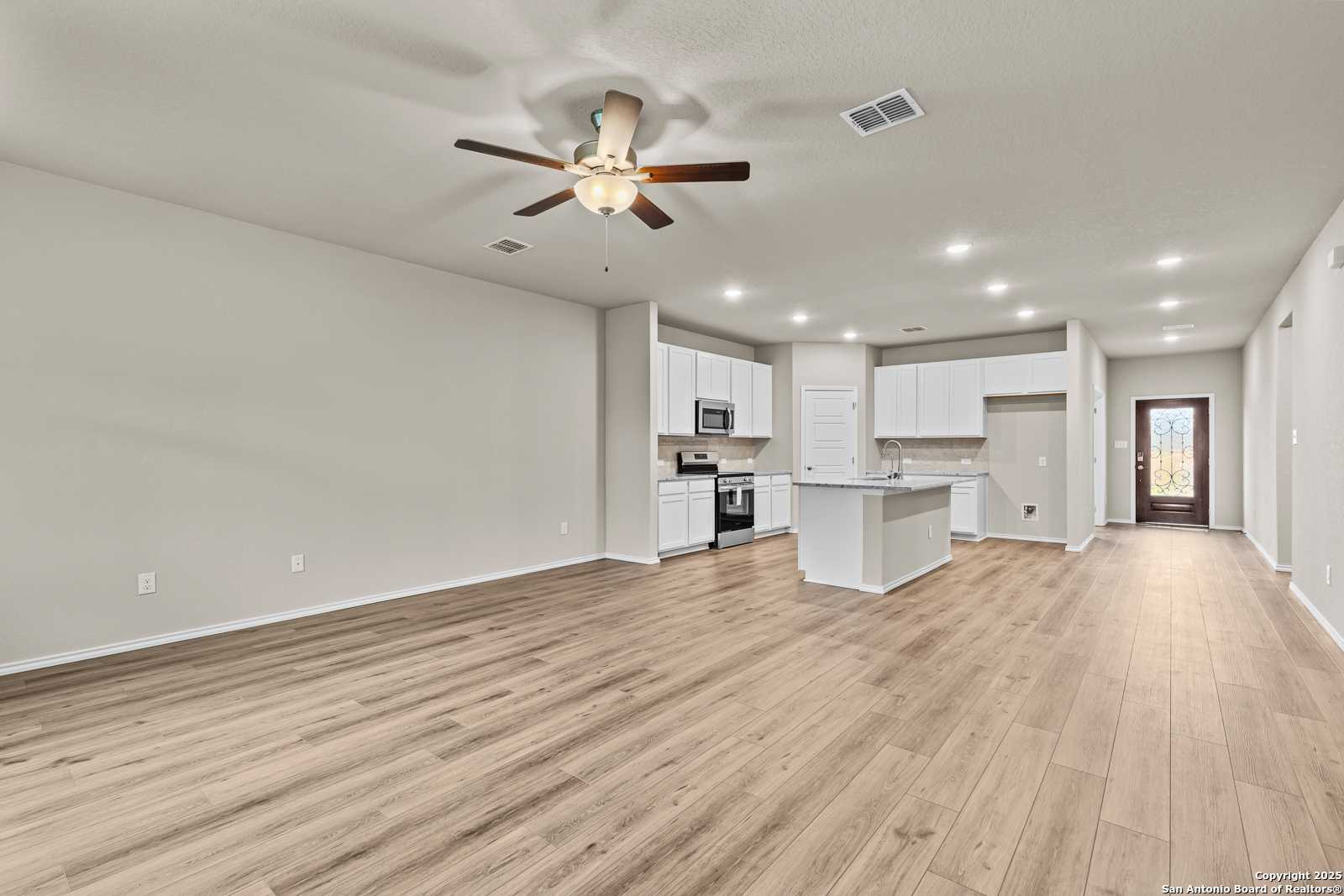 Modern open-concept kitchen with white island, stainless appliances, ceiling fan, and hardwood floors in Davidson Homes The Douglas F, San Antonio