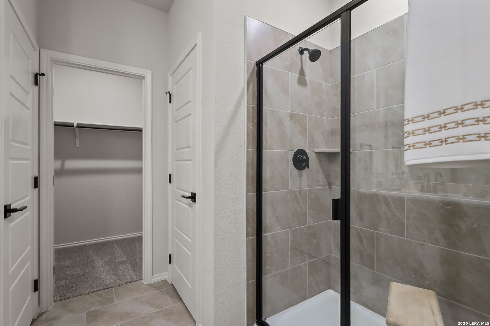 Modern master bathroom featuring frameless glass walk-in shower, tiled walls, and adjacent walk-in closet in Davidson Homes The Daphne H, Seguin, Texas