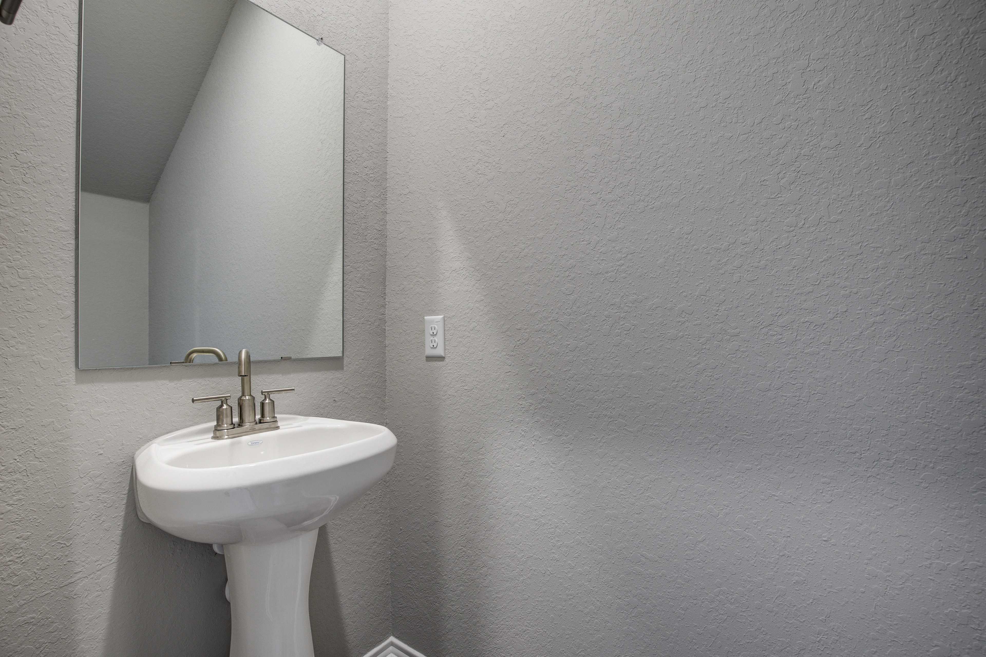 Modern powder room in The Blanco B showcasing white pedestal sink, bronze faucet, frameless mirror, and light gray walls