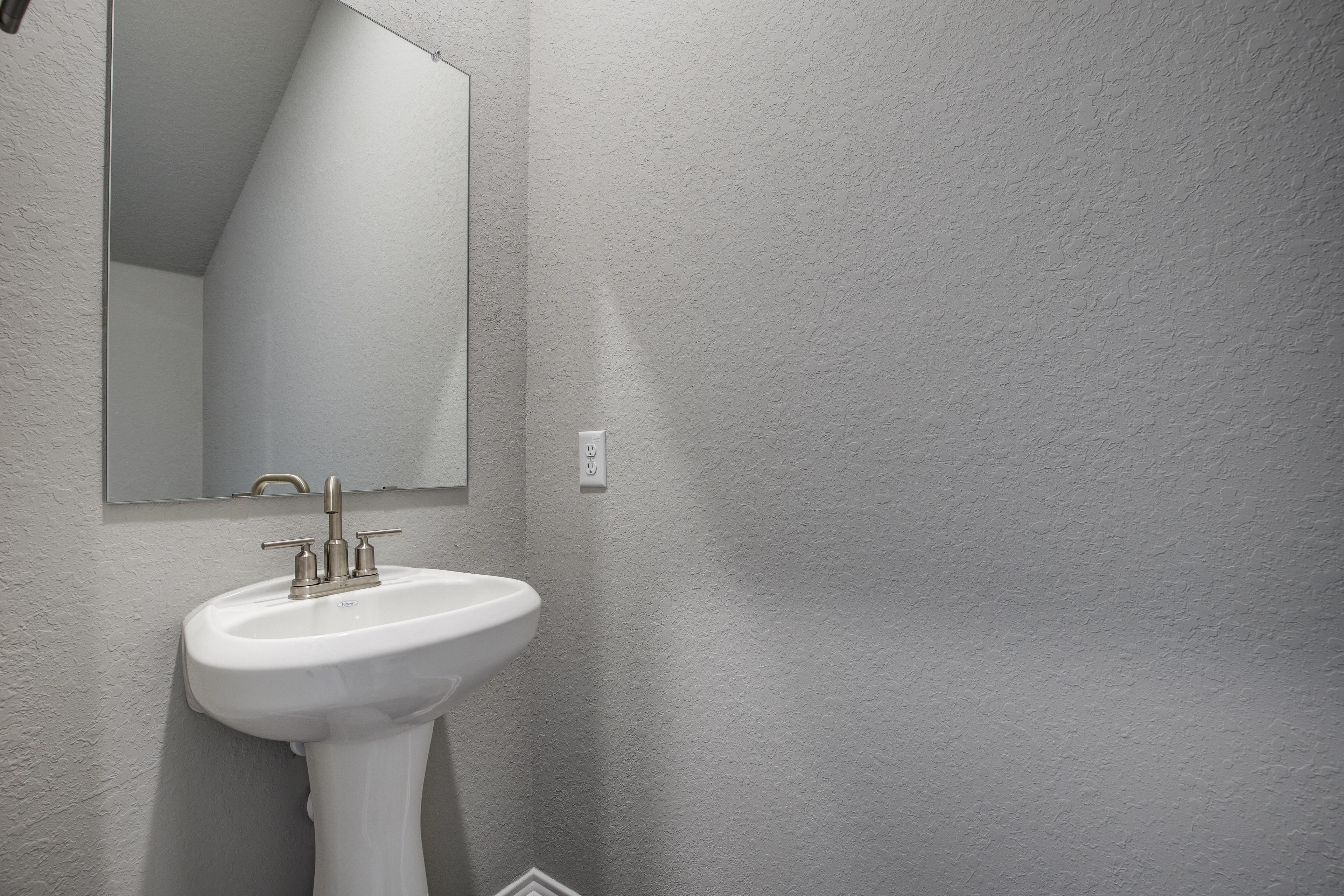 Modern powder room in The Blanco C with white pedestal sink, rectangular mirror, and gray textured walls