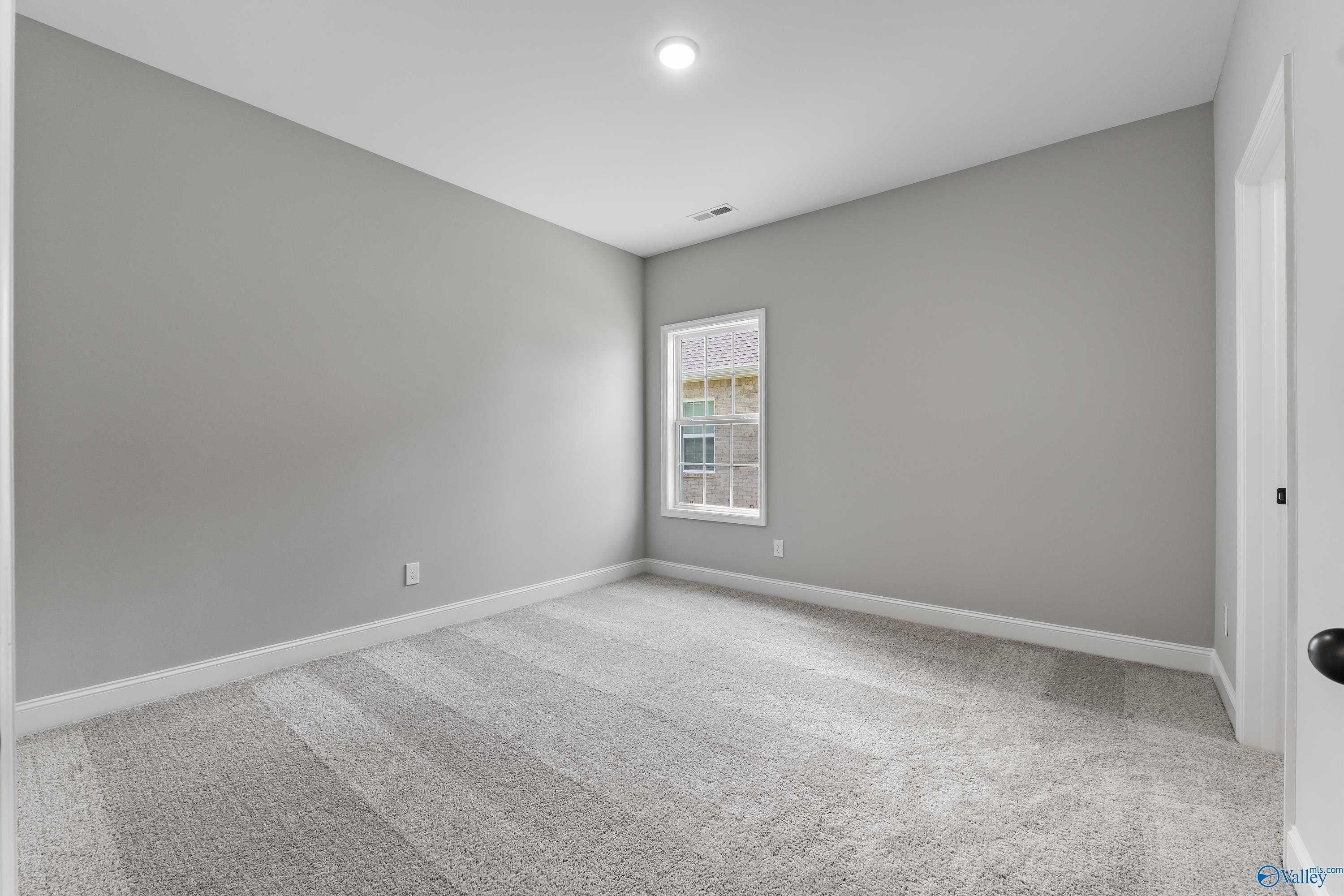 Bright secondary bedroom featuring light gray walls, plush carpet, and large window in Davidson Homes Montgomery B With Bonus, Toney, Alabama