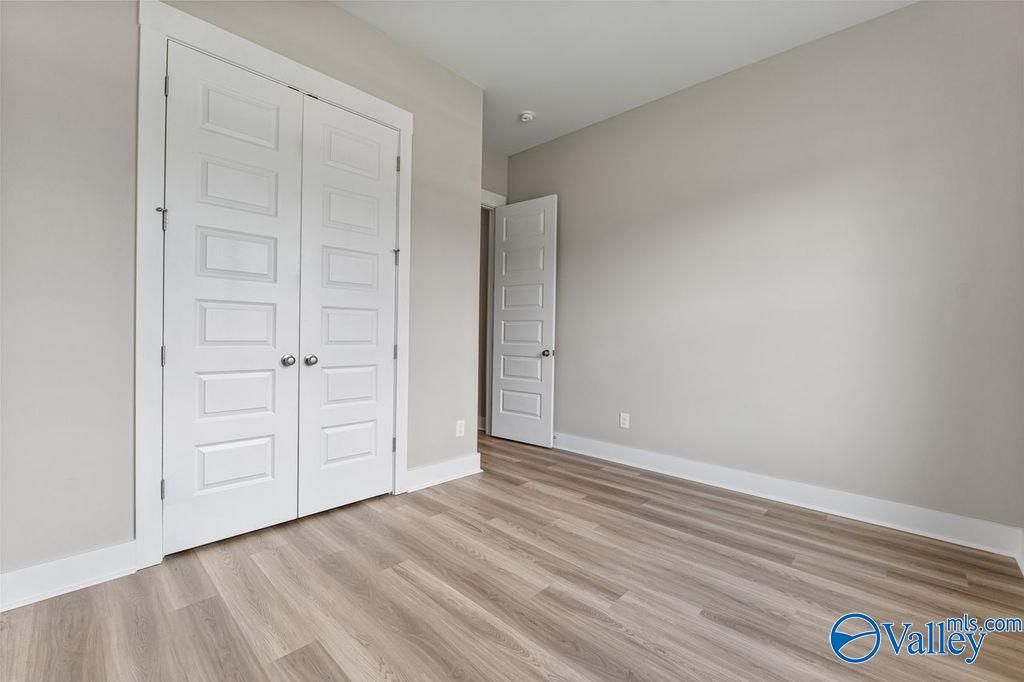 Spacious bedroom with white double closet doors, light gray walls, and luxury vinyl plank flooring in Evermore Homes The Oxford, Owens Cross Roads, Alabama