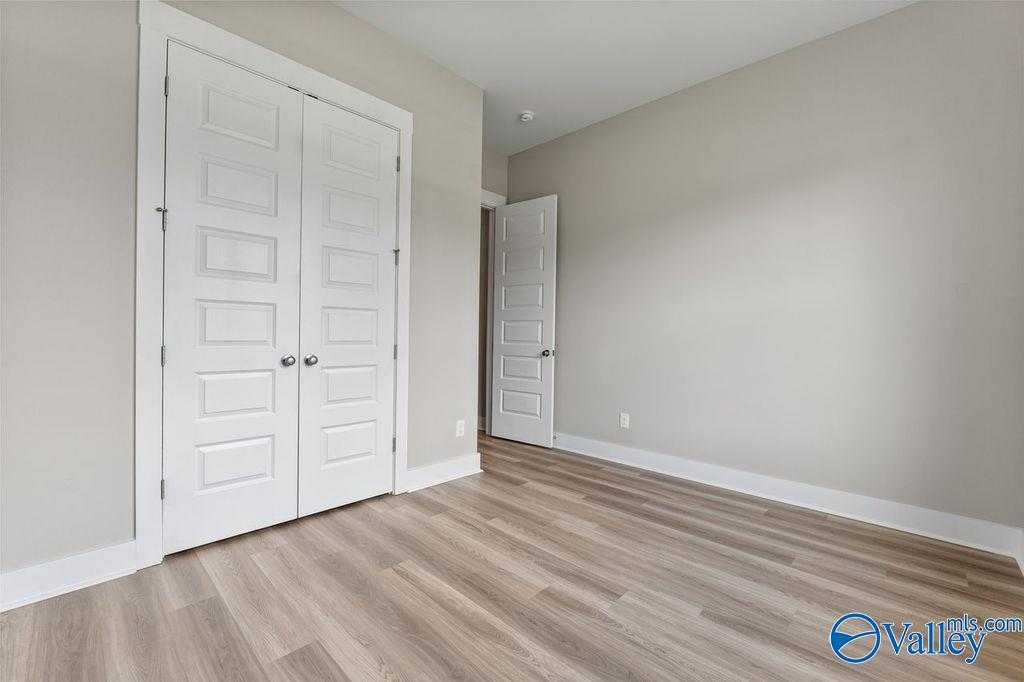 Spacious bedroom with white double closet doors, light gray walls, and luxury vinyl plank flooring in Evermore Homes The Oxford, Owens Cross Roads, Alabama