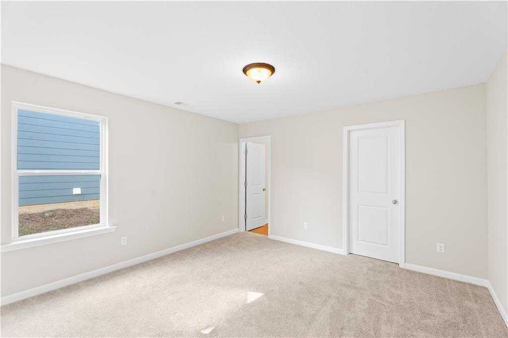 Bright secondary bedroom with beige walls, plush carpet, large window, and double doors in Davidson Homes The Washington, Phenix City, Alabama