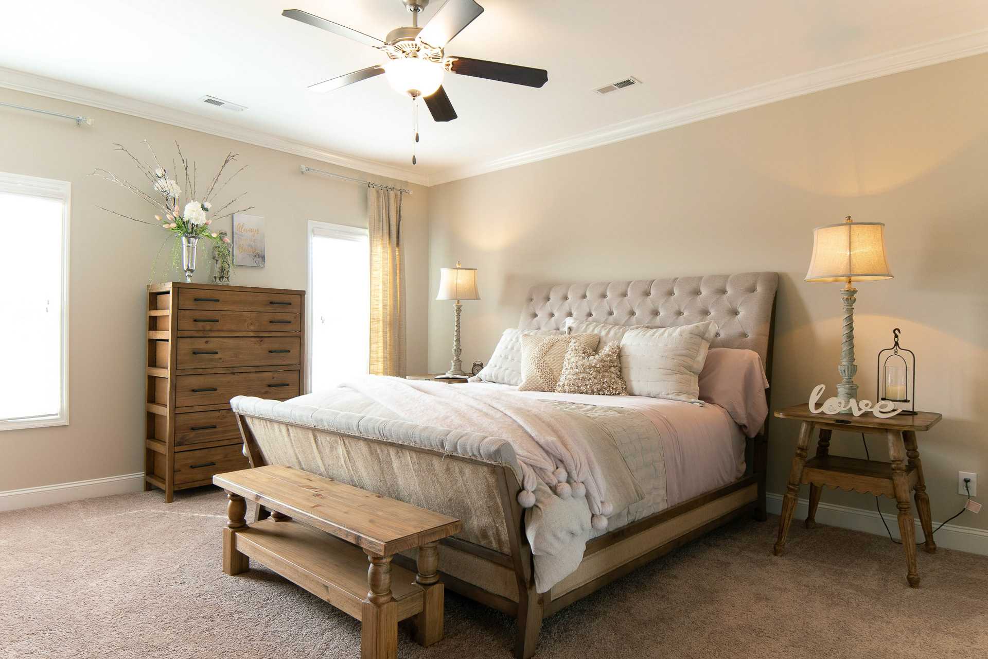 Master bedroom at The Dairy at Oak Grove in South Huntsville AL with tufted upholstered bed, wooden dresser, bench, and beige walls