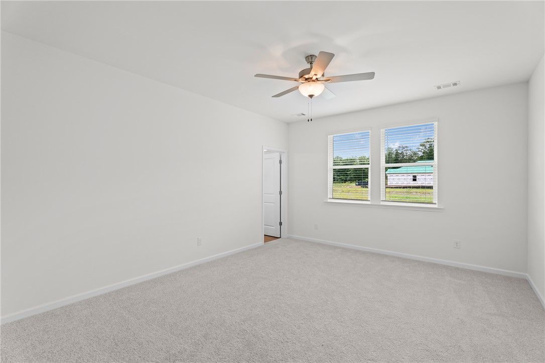 Bright, carpeted bedroom with ceiling fan in The Stella D floor plan by Evermore Homes at Silver Oak in Cusseta, Alabama.