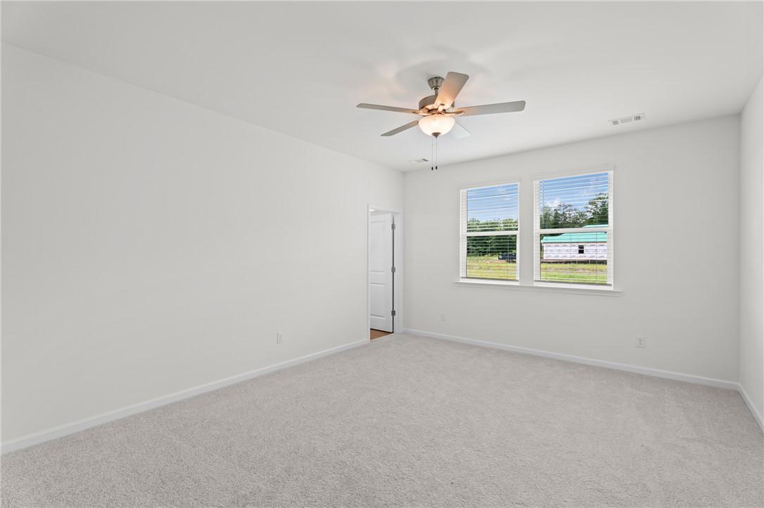 Bright, carpeted bedroom with ceiling fan in The Stella D floor plan by Evermore Homes at Silver Oak in Cusseta, Alabama.