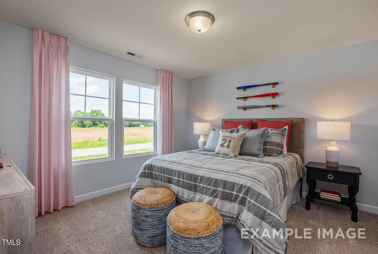Cozy bedroom with surfboard decor, queen bed, pink curtains, and field views in Davidson Homes The Willow G, Angier, NC