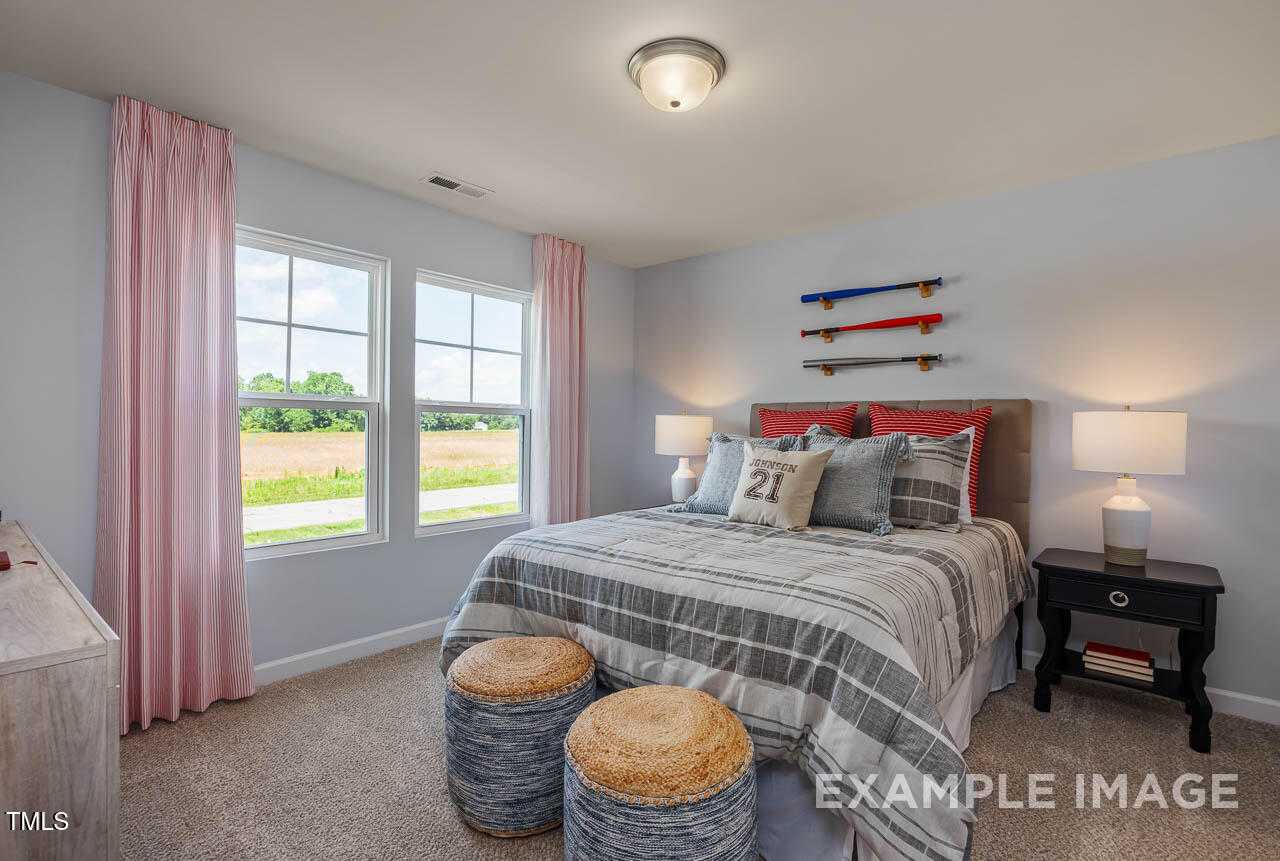 Cozy teen bedroom with queen bed, gray bedding, surfboard decor on light walls, large windows overlooking fields in Davidson Homes The Willow G, Angier, NC