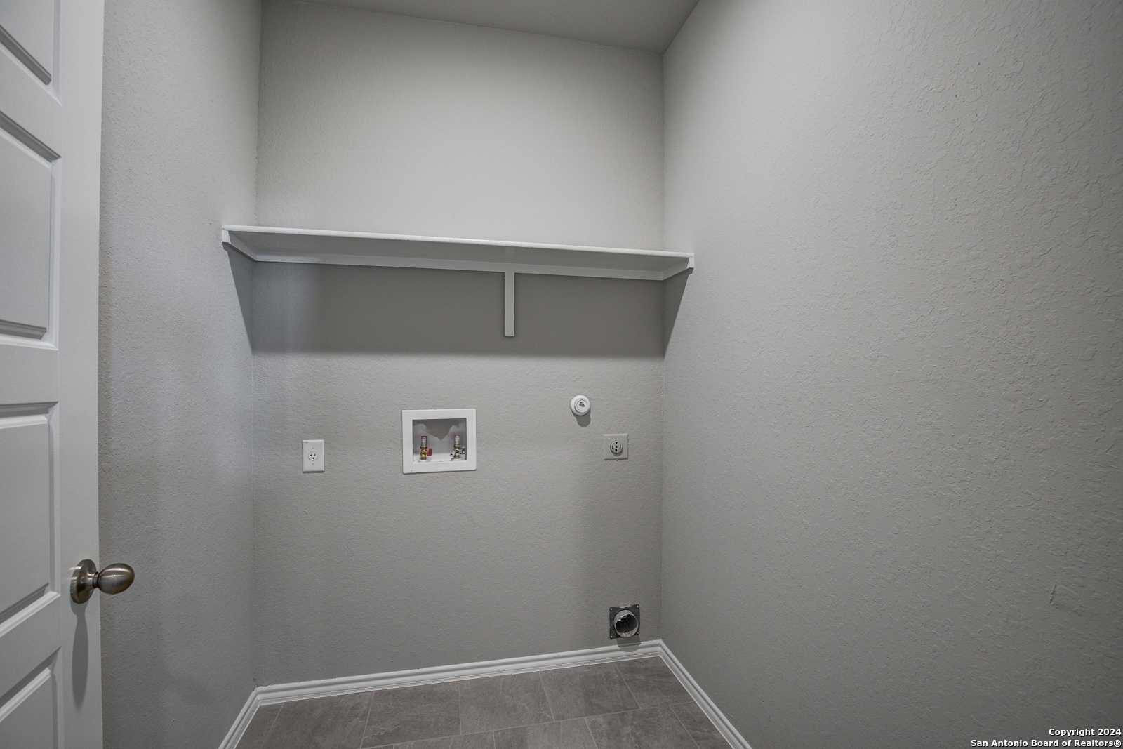 Neutral-toned laundry room with built-in shelves, utility sink, and washer-dryer hookups in Davidson Homes The Blanco C, San Antonio