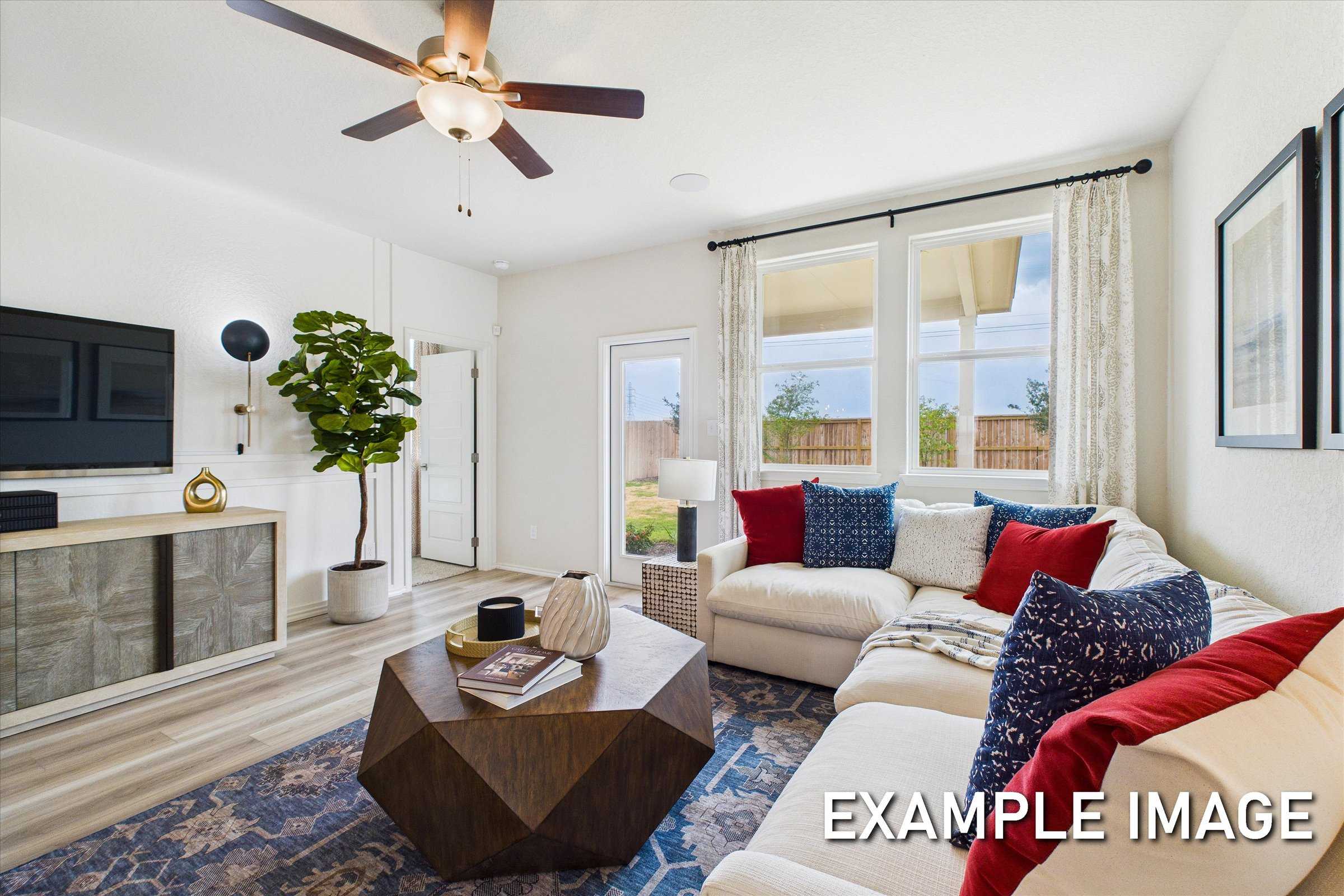 Spacious living room with L-shaped white sofa, wooden coffee table, ceiling fan, and garden view in Davidson Homes The Brazos C, San Antonio