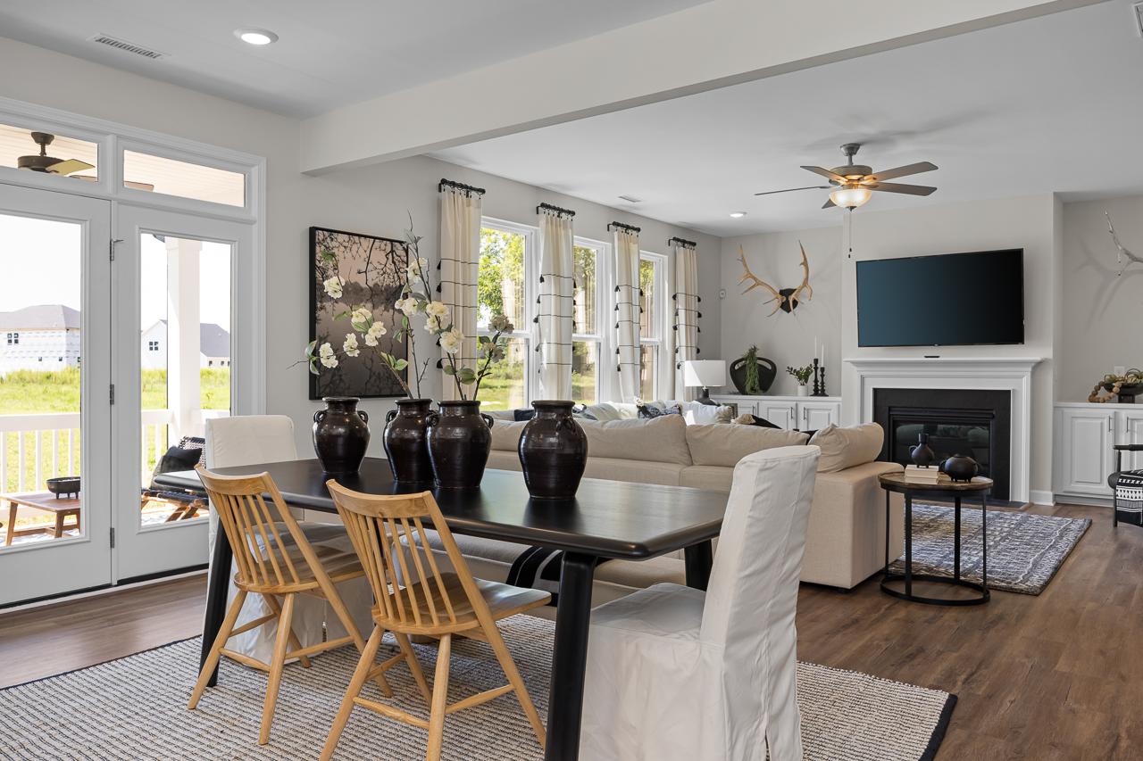 Open-concept dining living area at Wellers Knoll in Lillington NC with hardwood floors, wooden table, beige sofa, and fireplace