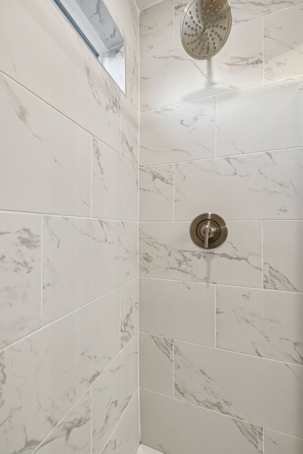 Modern walk-in shower with white marble subway tiles, rainfall showerhead, and niche in The Willow master bath, Davidson Homes