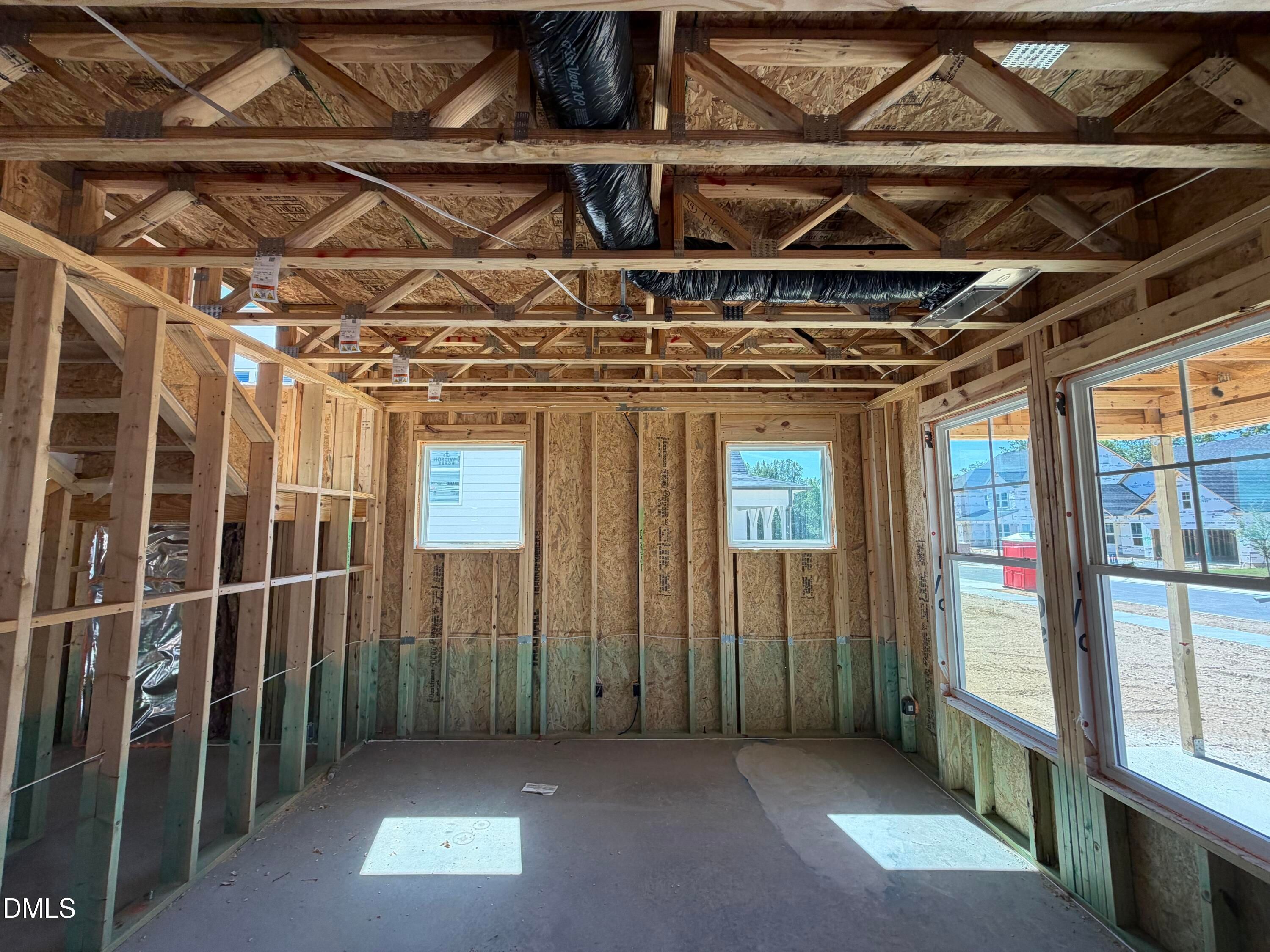 Unfinished framed interior room with exposed wood trusses and ductwork in new construction home by Davidson Homes in Wendell, NC