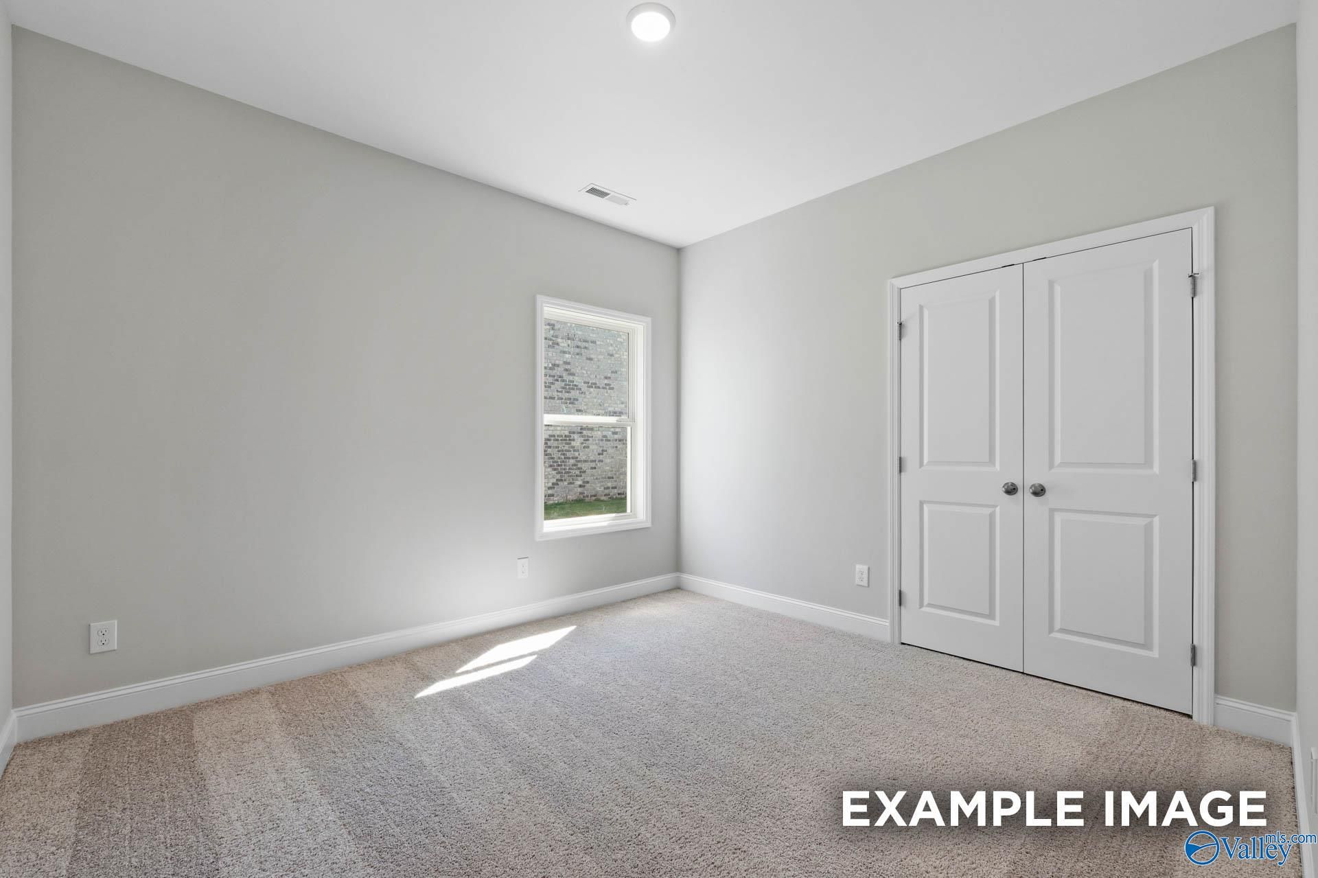 Bright bedroom with neutral carpet and double-door closet in The Everett B floor plan at The Meadows in Athens, Alabama.