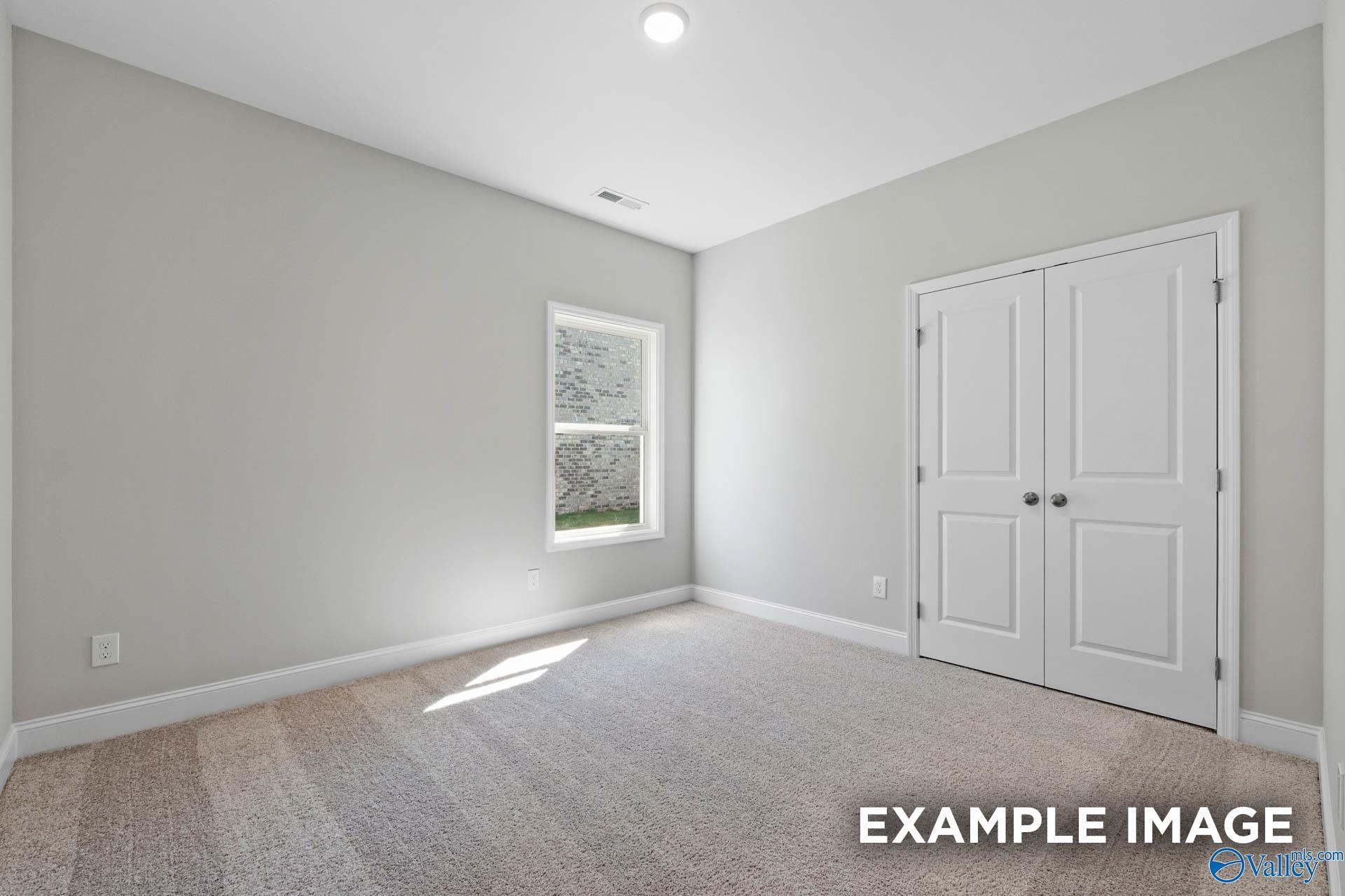 Bright bedroom with neutral carpet and double-door closet in The Everett B floor plan at The Meadows in Athens, Alabama.