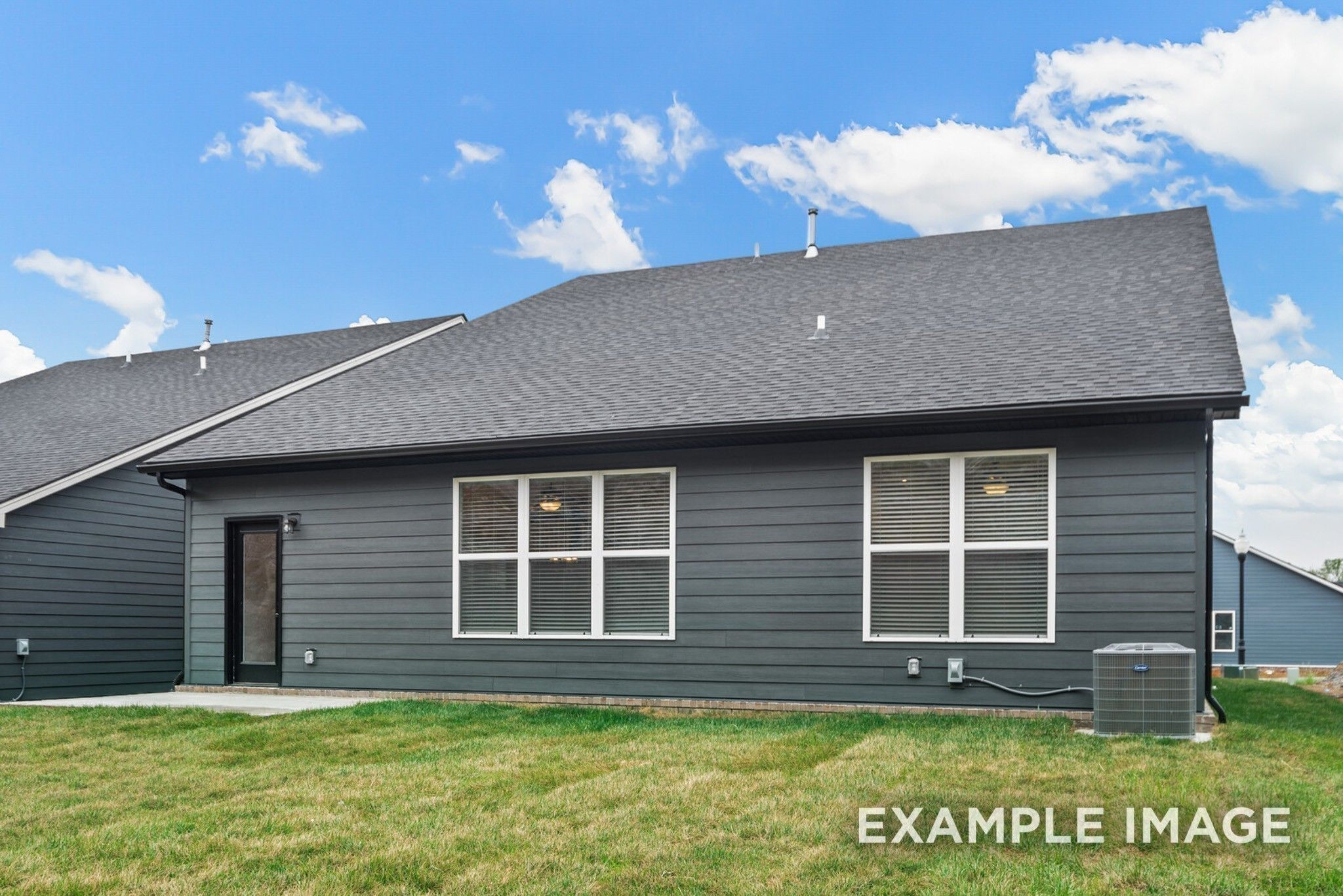 Rear view of 2-story gray-sided 5-bedroom home with large windows, back door, and grassy yard in Woods Crossing, Gallatin, Tennessee