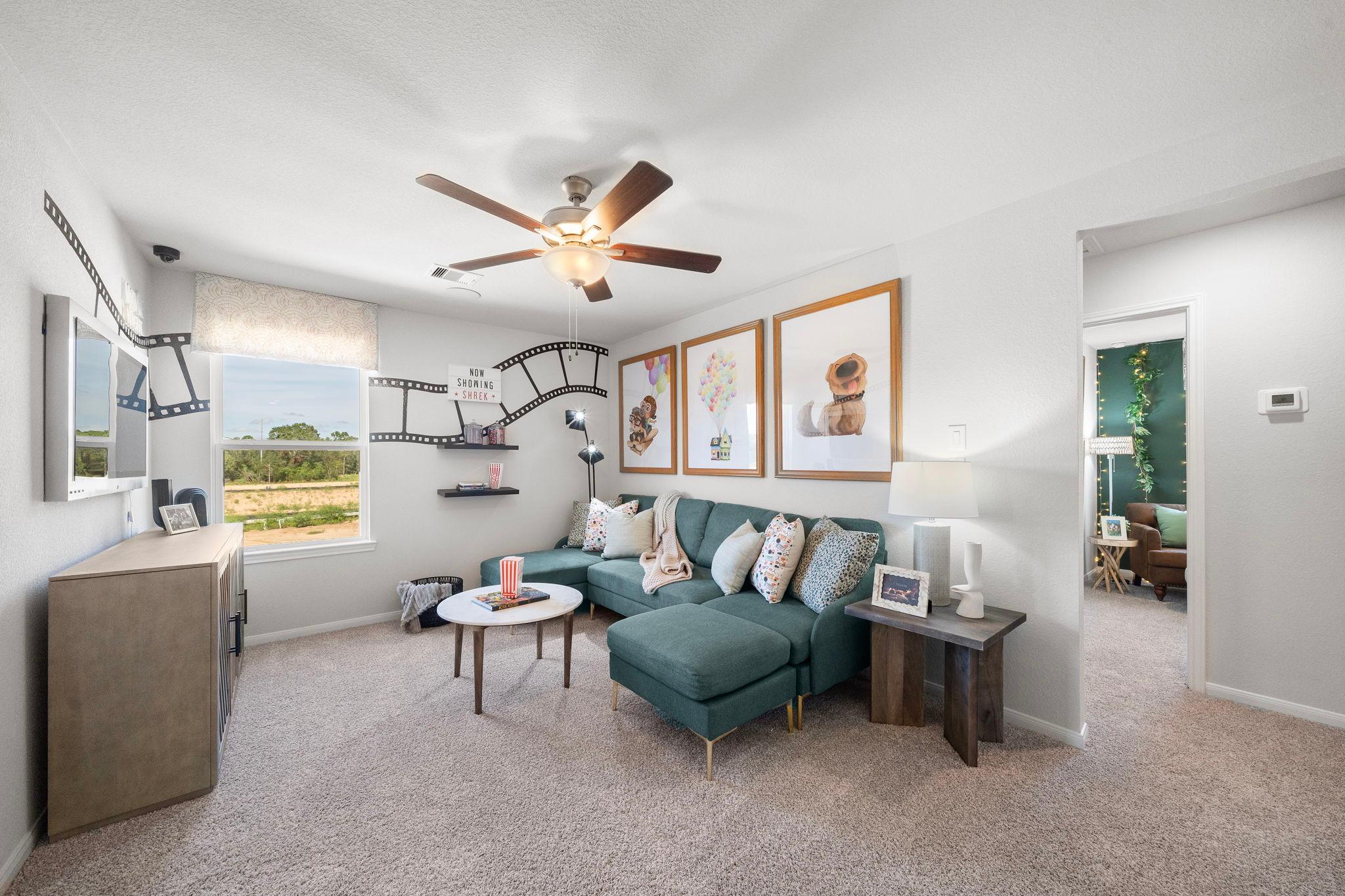 Cozy loft bonus room at Caney Creek Place in Conroe TX with teal sectional sofa, movie-themed wall decor, ceiling fan, and scenic window view