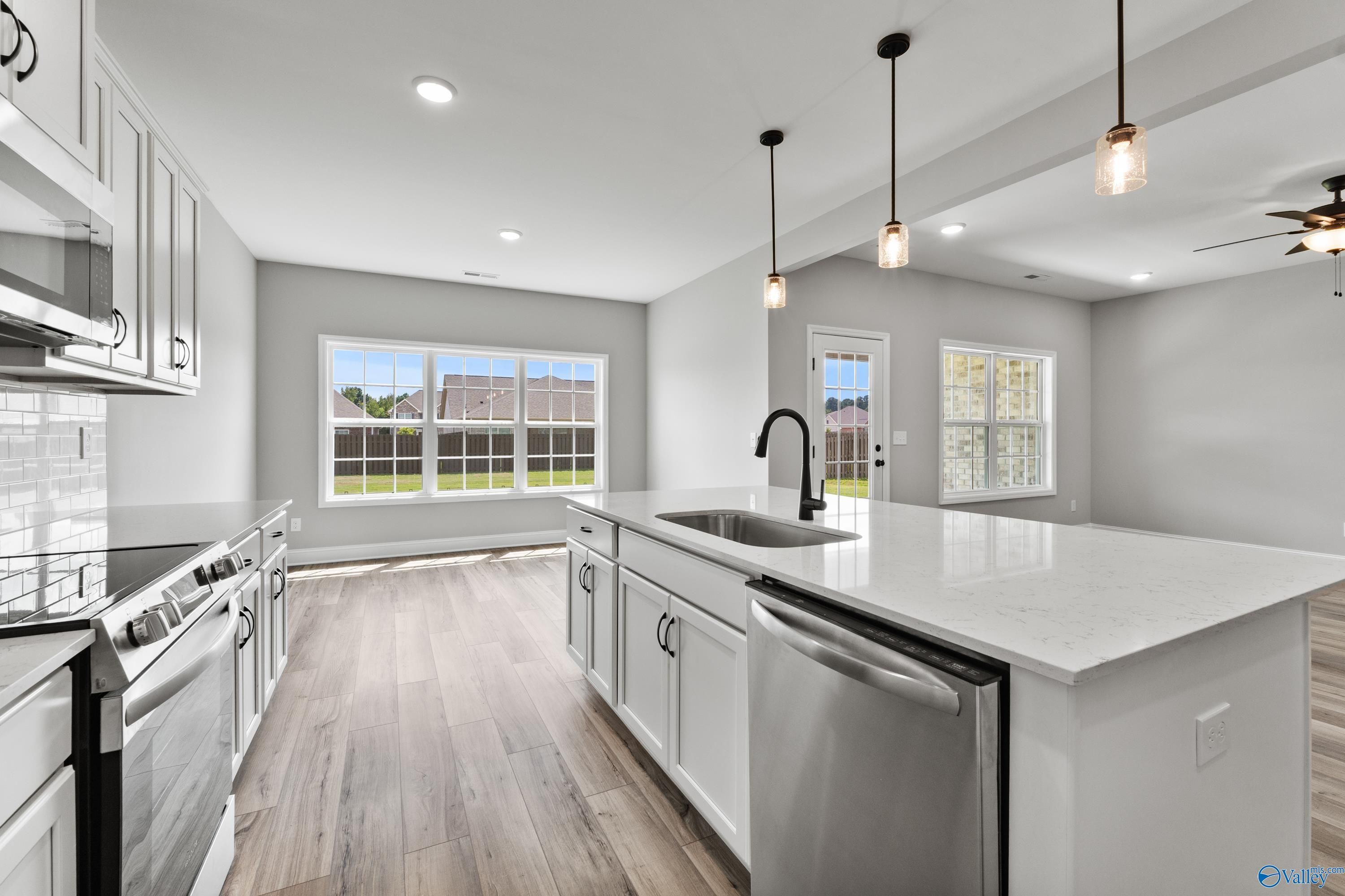 Modern white kitchen with quartz island sink, stainless appliances, subway tile, and backyard view in Davidson Homes Montgomery B, Toney AL