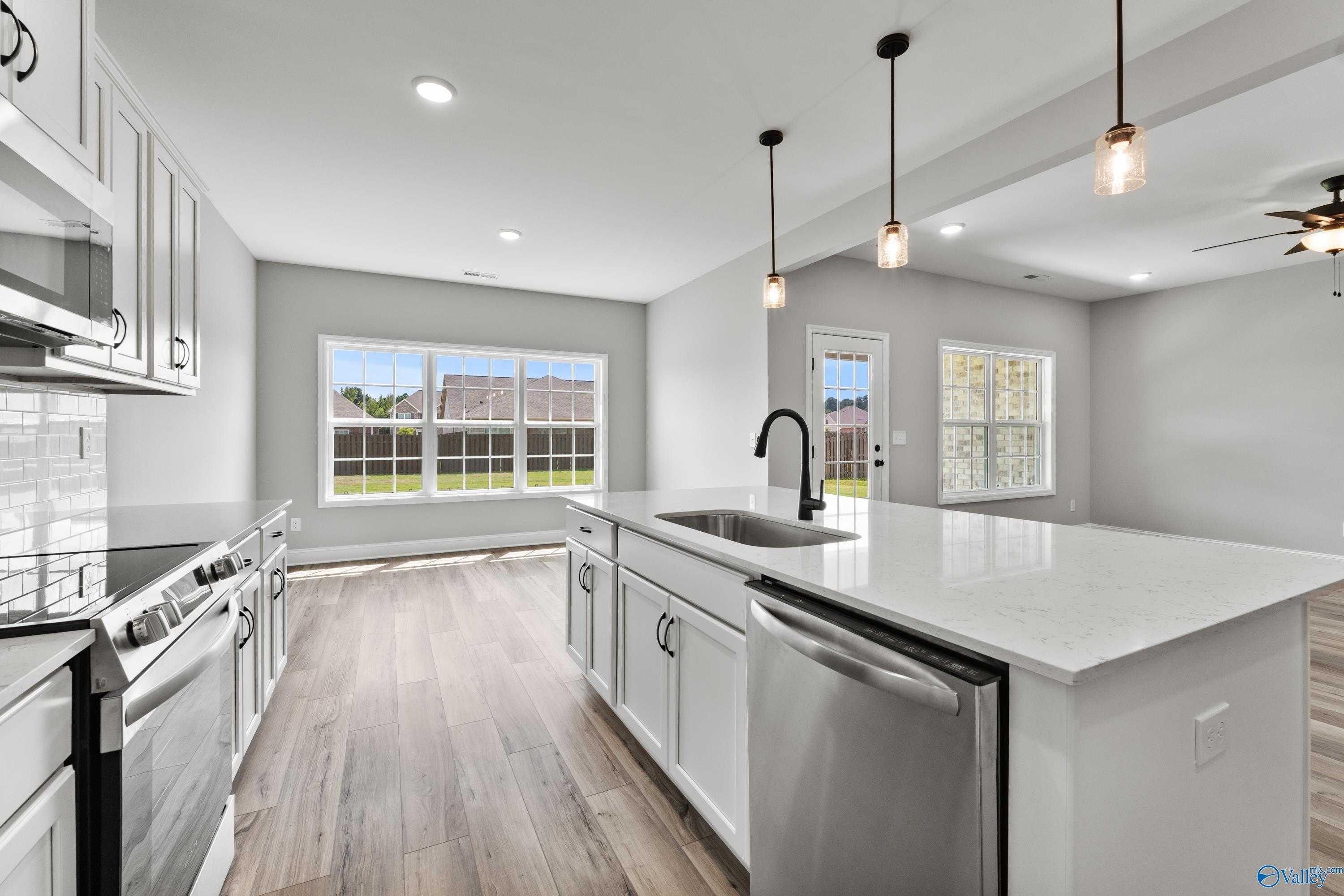 Modern white kitchen with quartz island sink, stainless appliances, subway tile, and backyard view in Davidson Homes Montgomery B, Toney AL