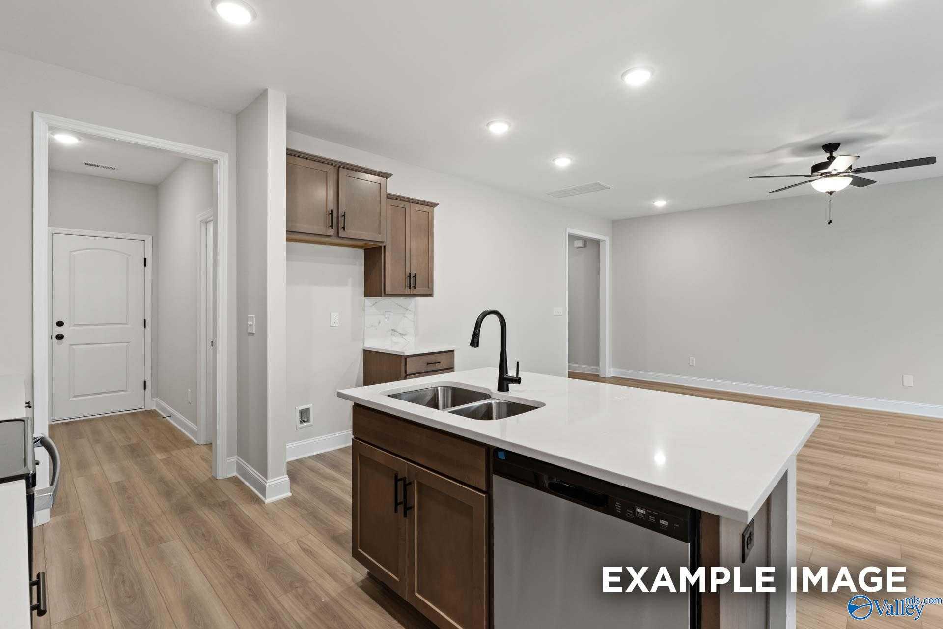 Modern kitchen featuring white quartz island, brown shaker cabinets, stainless dishwasher in The Camden D by Davidson Homes, Huntsville AL