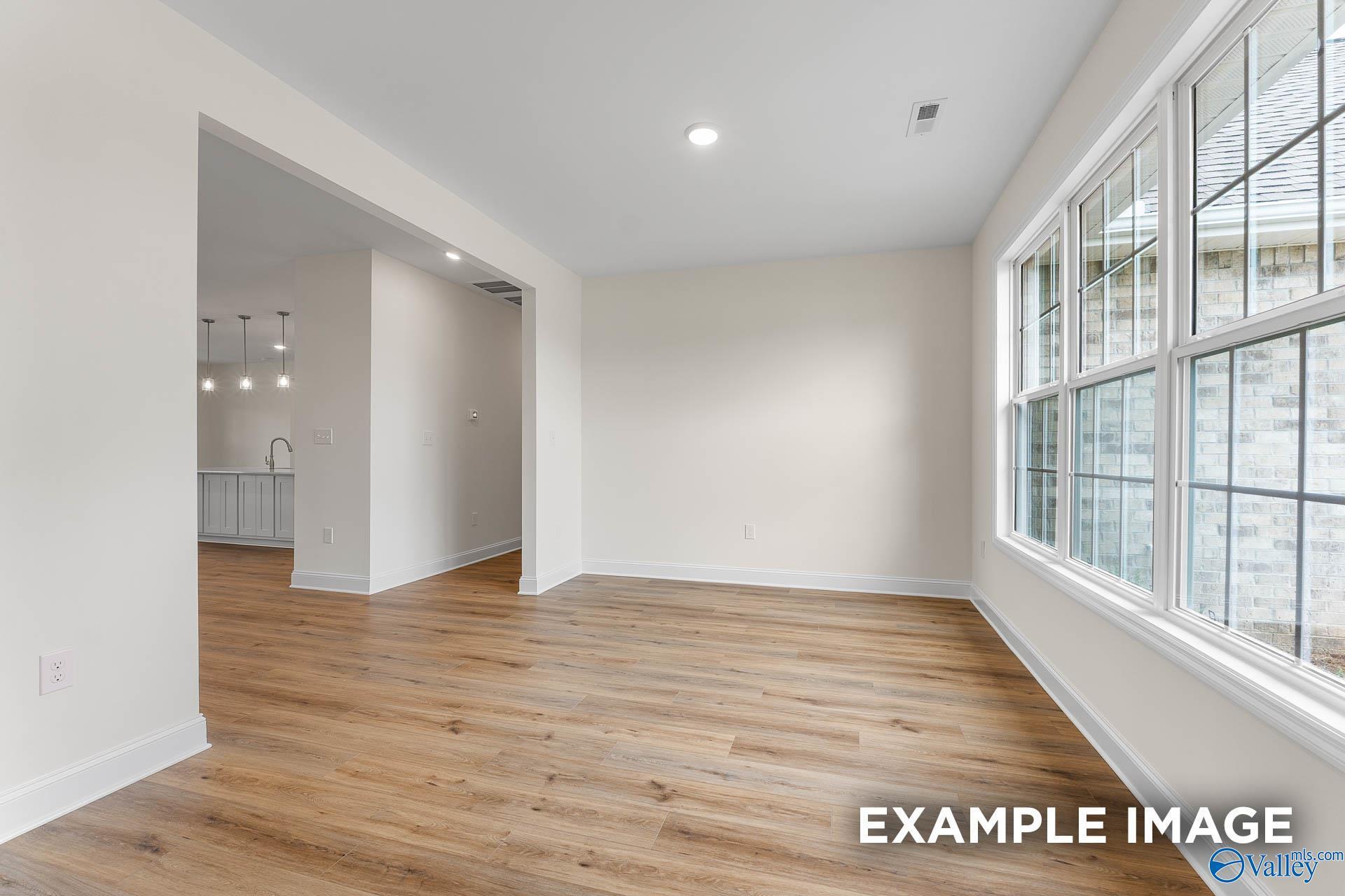 Bright open-concept family room with hardwood floors, large windows, and adjacent kitchen in Davidson Homes The Emory, Toney, Alabama