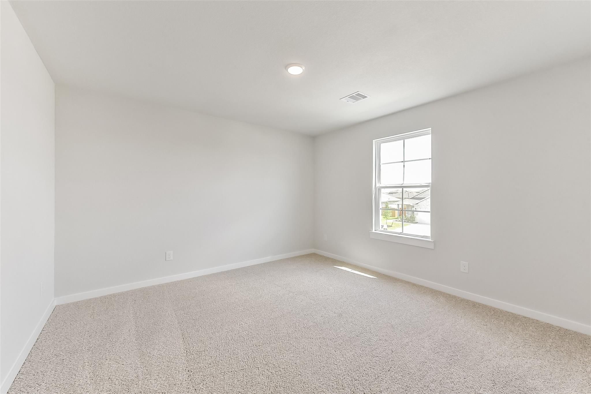 Bright empty bedroom with large window, neutral gray walls, and beige carpet in Davidson Homes The Tierra C, Dayton, Texas