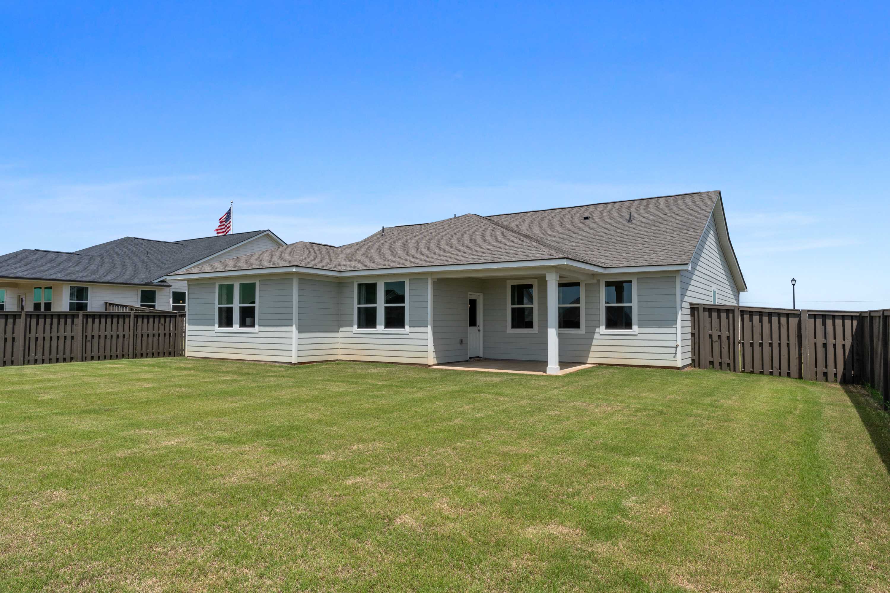 Spacious backyard of single-story home at Anderson Farm in Athens Alabama with covered patio, lush green lawn, and privacy fence