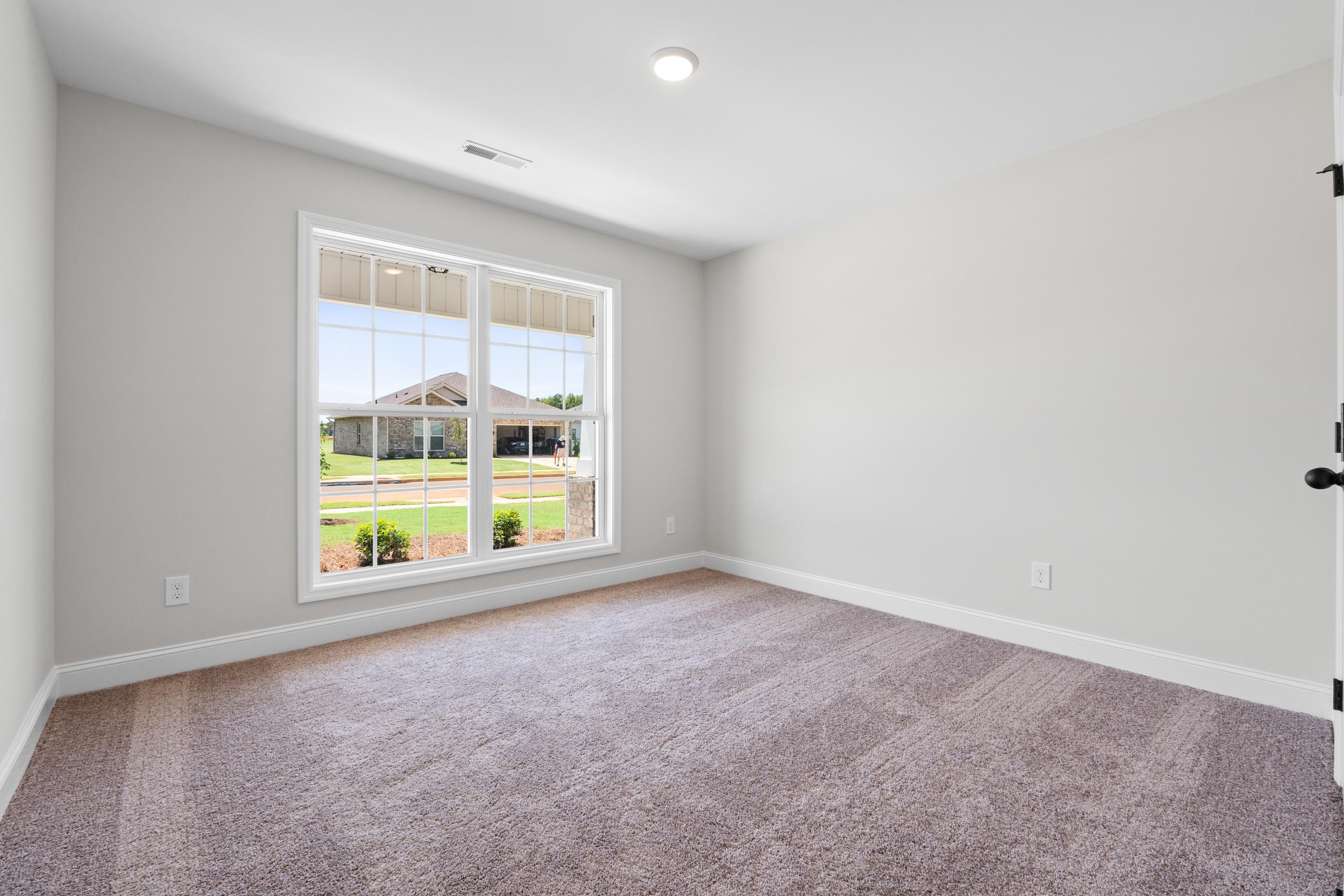 Spacious empty bedroom in The Everett home design with large window overlooking green lawn and backyard view