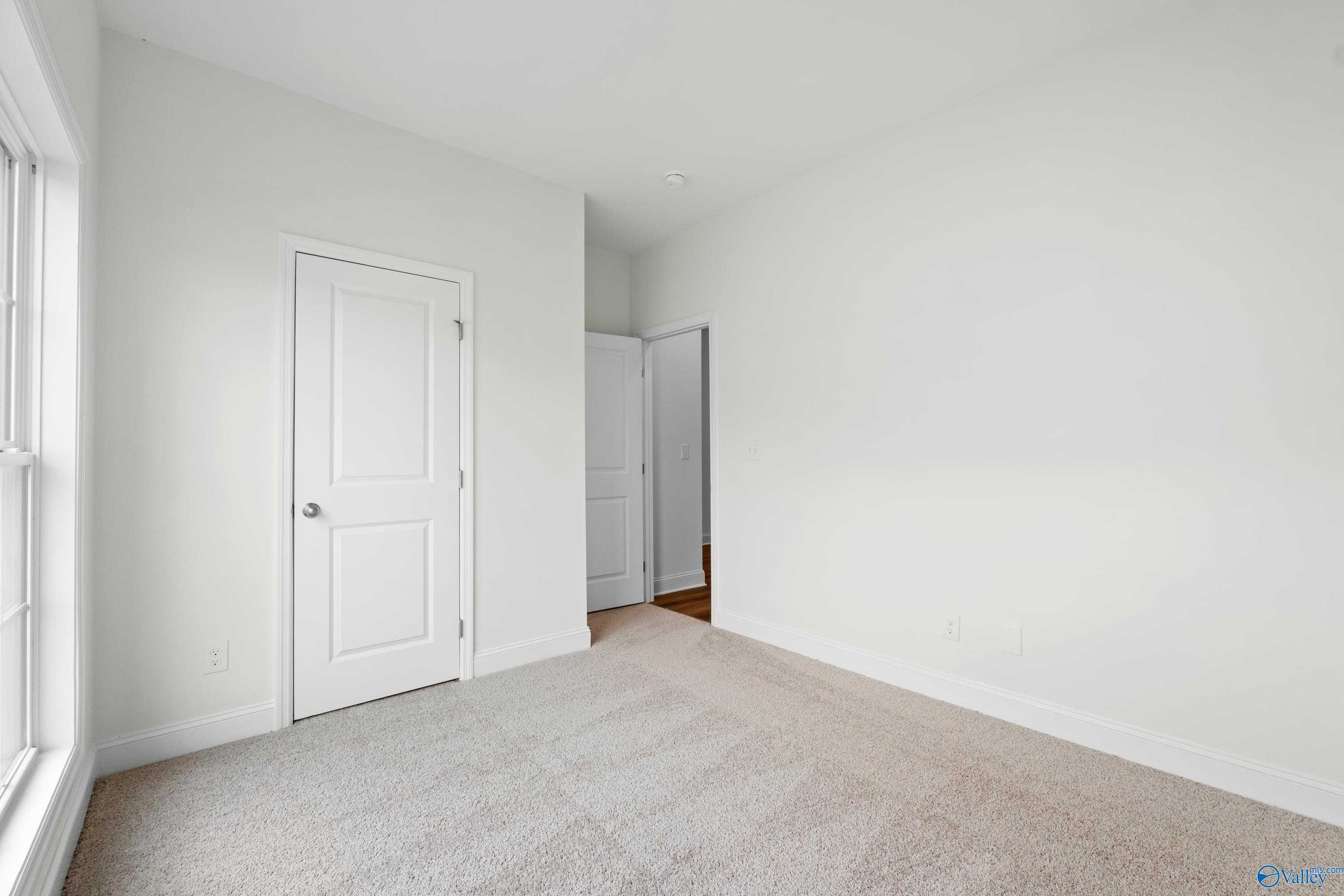 Bright secondary bedroom with beige carpet, white doors, large window in The Asheville C by Davidson Homes, Athens, Alabama