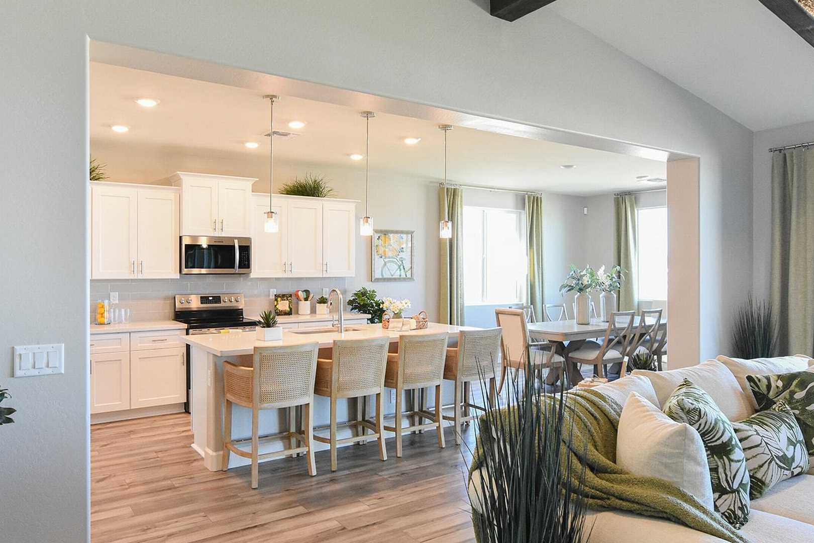 Open-concept kitchen in The Summit B with white cabinets, large island bar stools, adjacent dining area, and living room sofa, Evermore Homes design