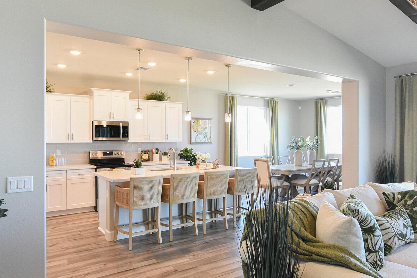 Spacious open-concept kitchen in The Summit E featuring white cabinets, large island with bar stools, adjacent dining area, and living room by Evermore Homes