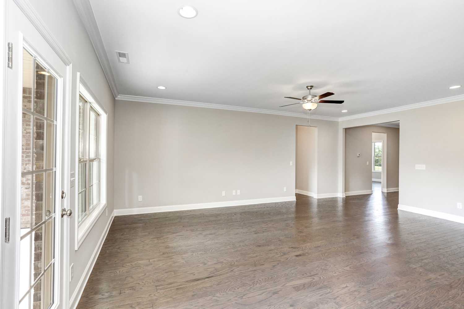 Spacious open-concept living room in The Montgomery home with hardwood floors, ceiling fan, and large windows