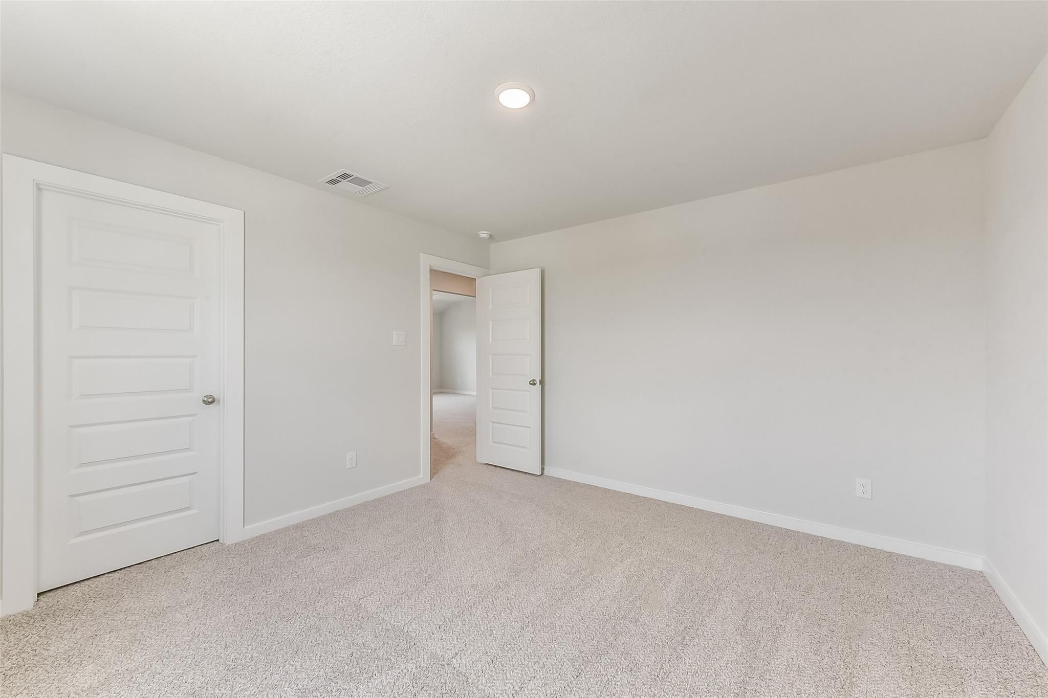Spacious empty bedroom with beige carpet, white walls and doors in Davidson Homes The Tierra C, Dayton, Texas