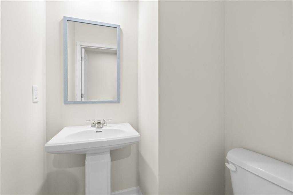 Elegant powder room featuring white pedestal sink, framed mirror, and toilet in Davidson Homes The Marion B, Kennesaw, Georgia