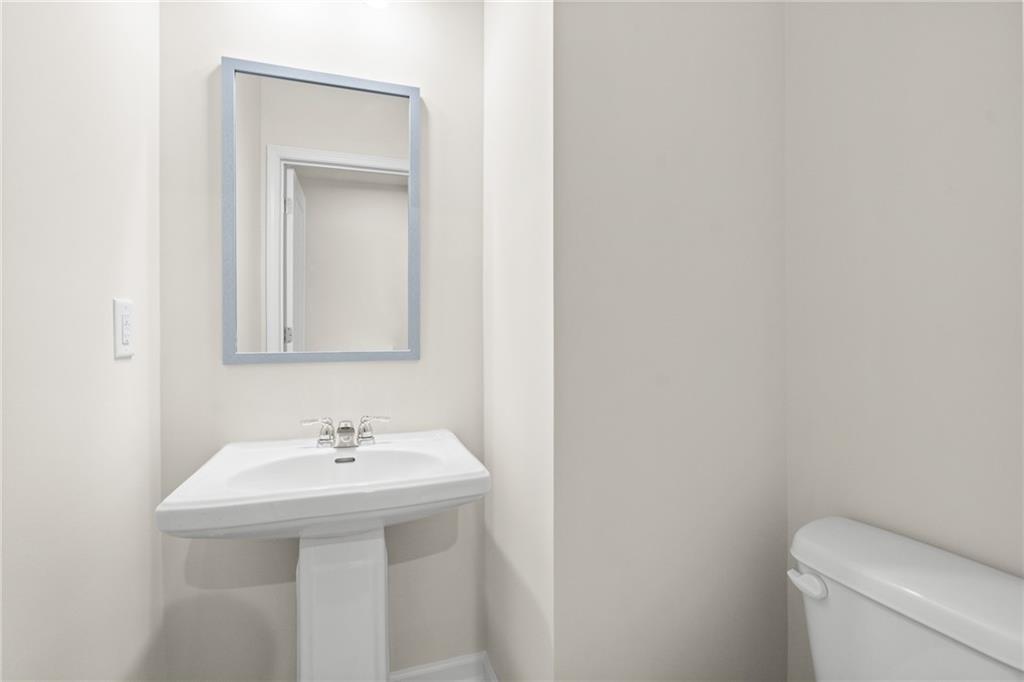 Elegant powder room featuring white pedestal sink, framed mirror, and toilet in Davidson Homes The Marion B, Kennesaw, Georgia