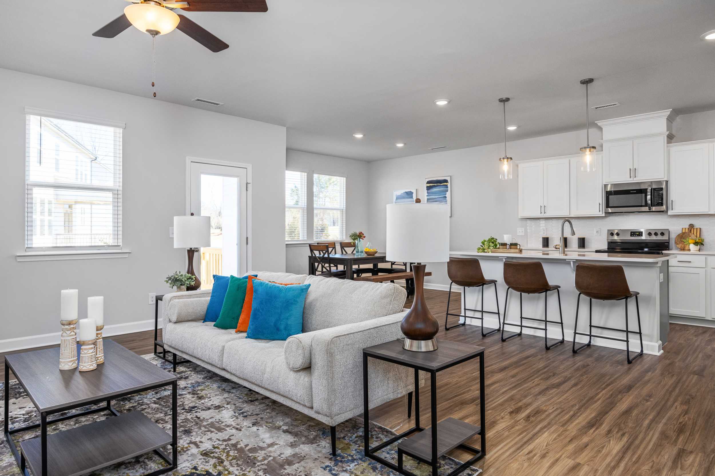 Open-concept living room and kitchen at Gregory Village Townhomes in Lillington NC with hardwood floors, white island, and gray sofa