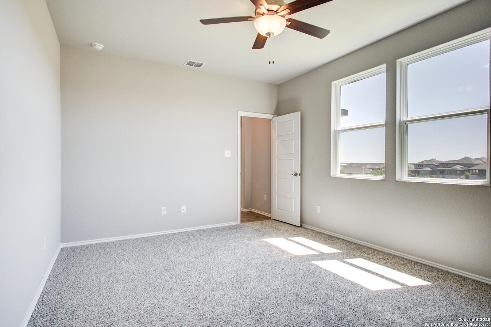 Bright secondary bedroom with ceiling fan, large sunny windows, and plush carpet in Davidson Homes The Douglas G, San Antonio
