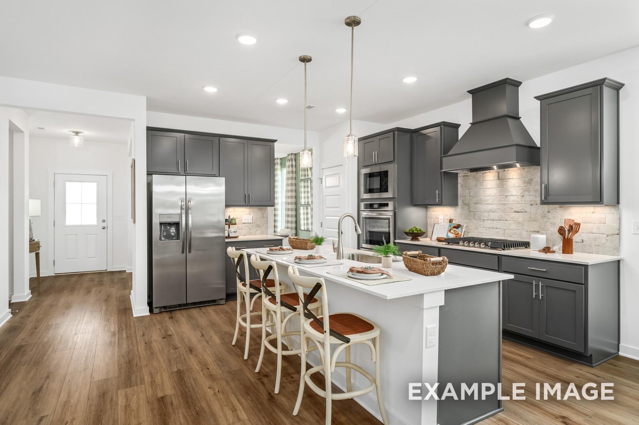 Modern kitchen with gray cabinets, center island, and stainless steel appliances in The Ash A plan at Woods Crossing.