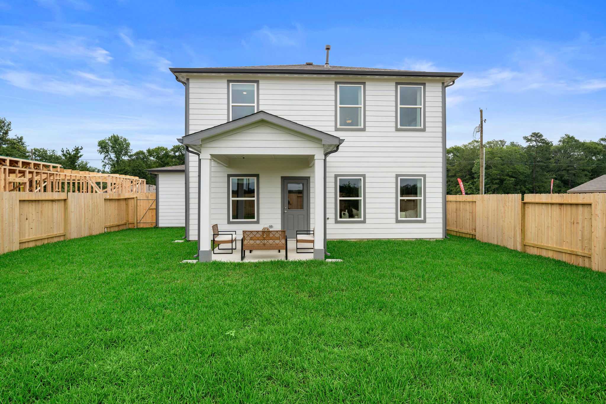 Spacious backyard of modern white home at Hill & Dale Ranch in Splendora Texas with covered porch, wooden benches, and lush green lawn