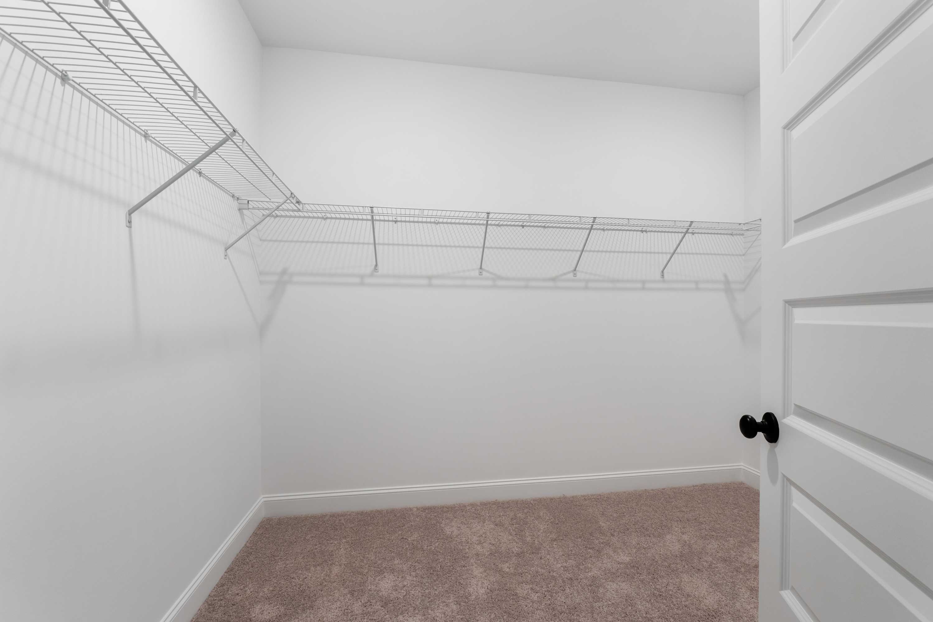 Spacious master walk-in closet in The Oxford home with wire shelving, white walls, and beige carpet
