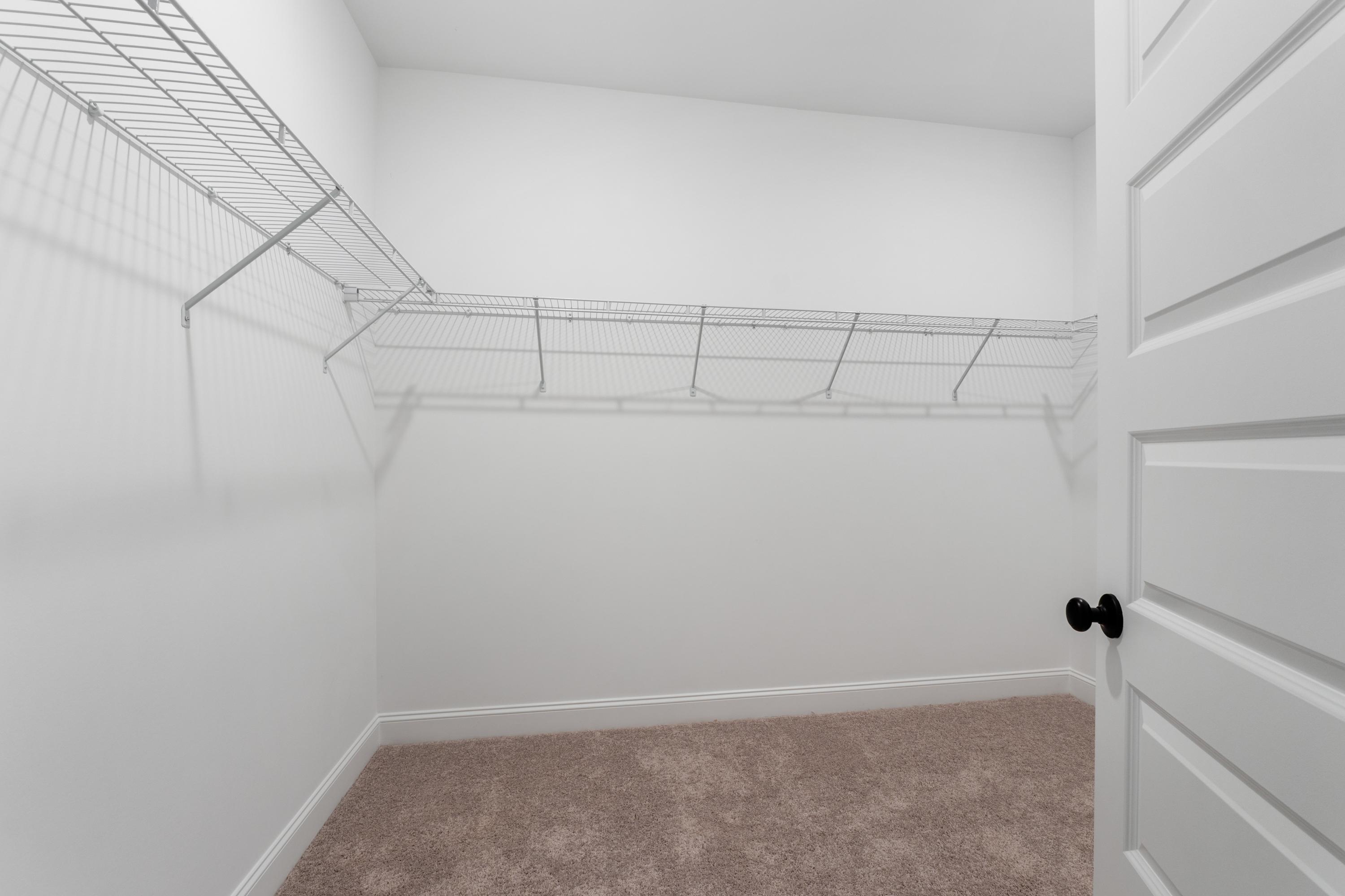 Spacious master walk-in closet in The Oxford home with wire shelving, white walls, and beige carpet