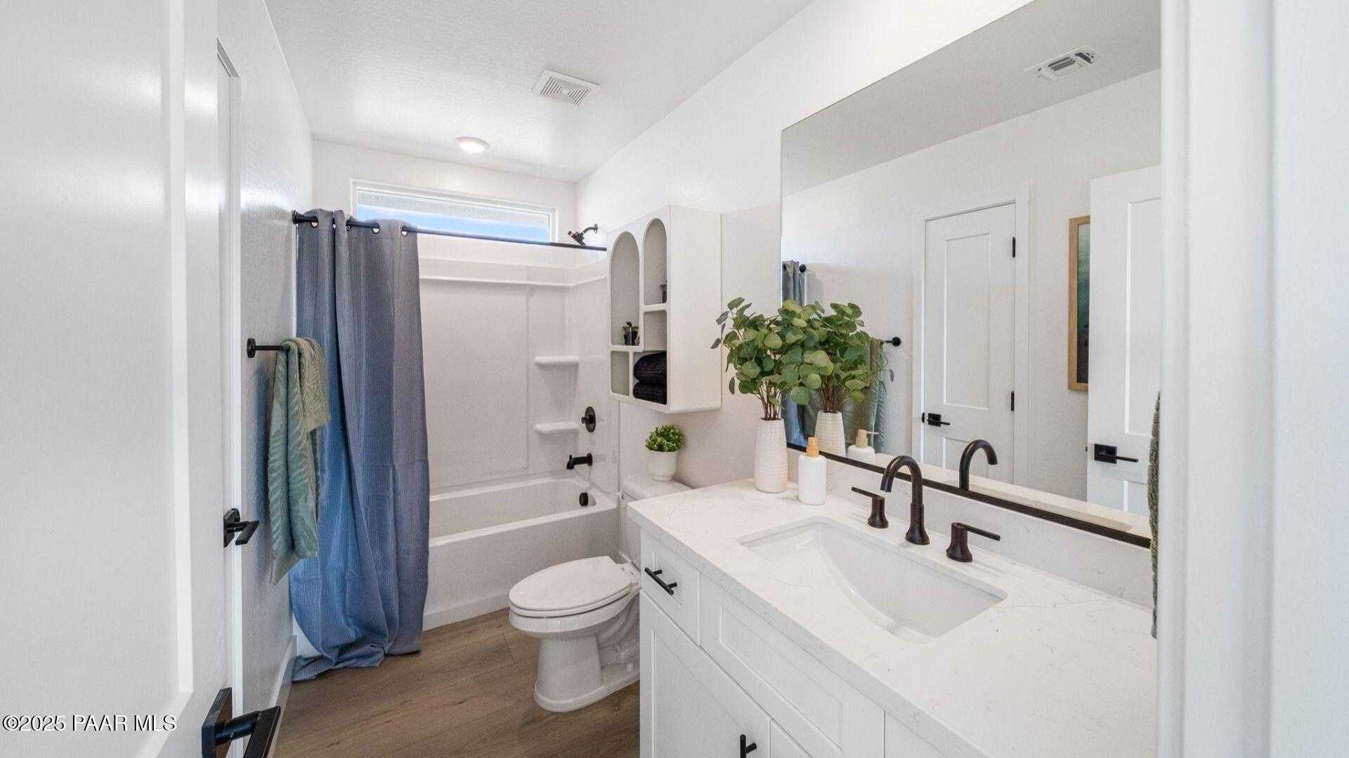 Elegant bathroom with white vanity, soaking tub, blue shower curtain, and potted plants in Davidson Homes Wilmington B, Prescott Arizona