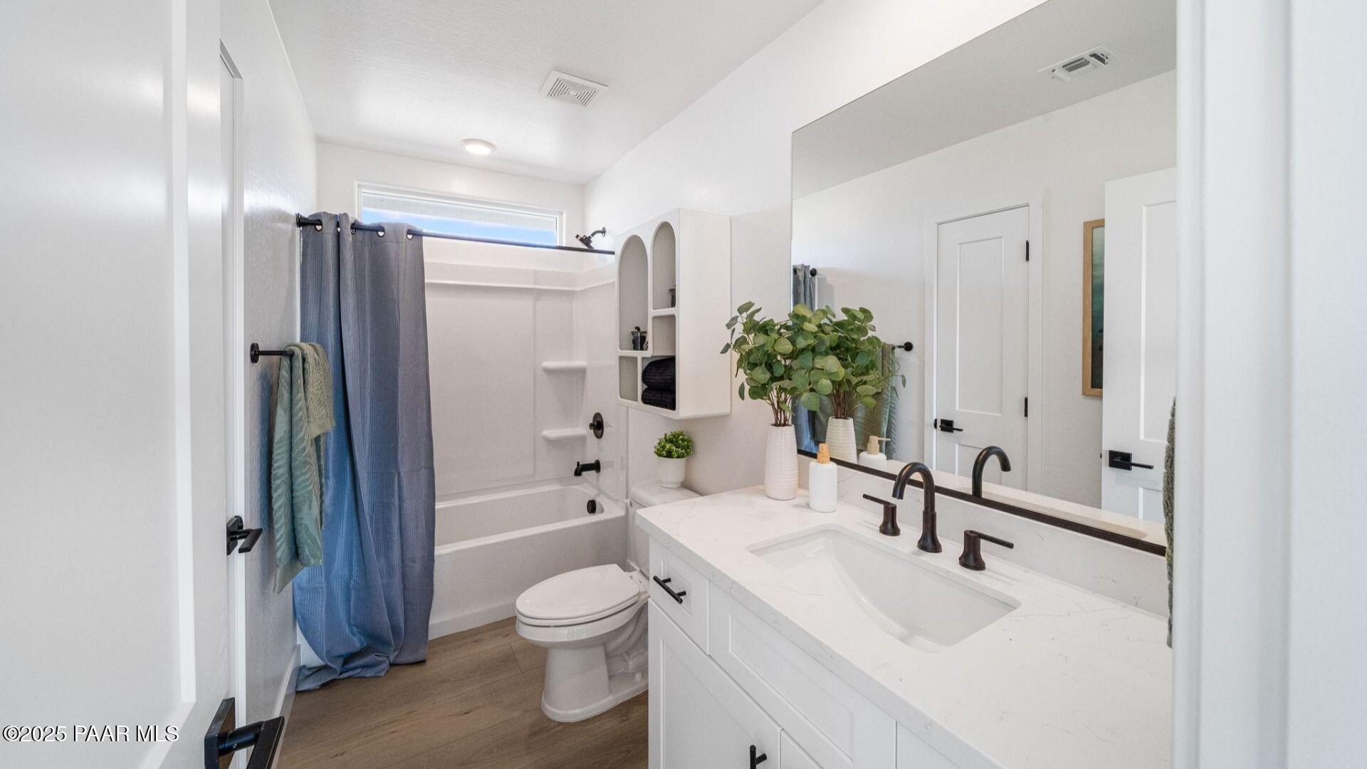 Elegant bathroom with white vanity, soaking tub, blue shower curtain, and potted plants in Davidson Homes Wilmington B, Prescott Arizona