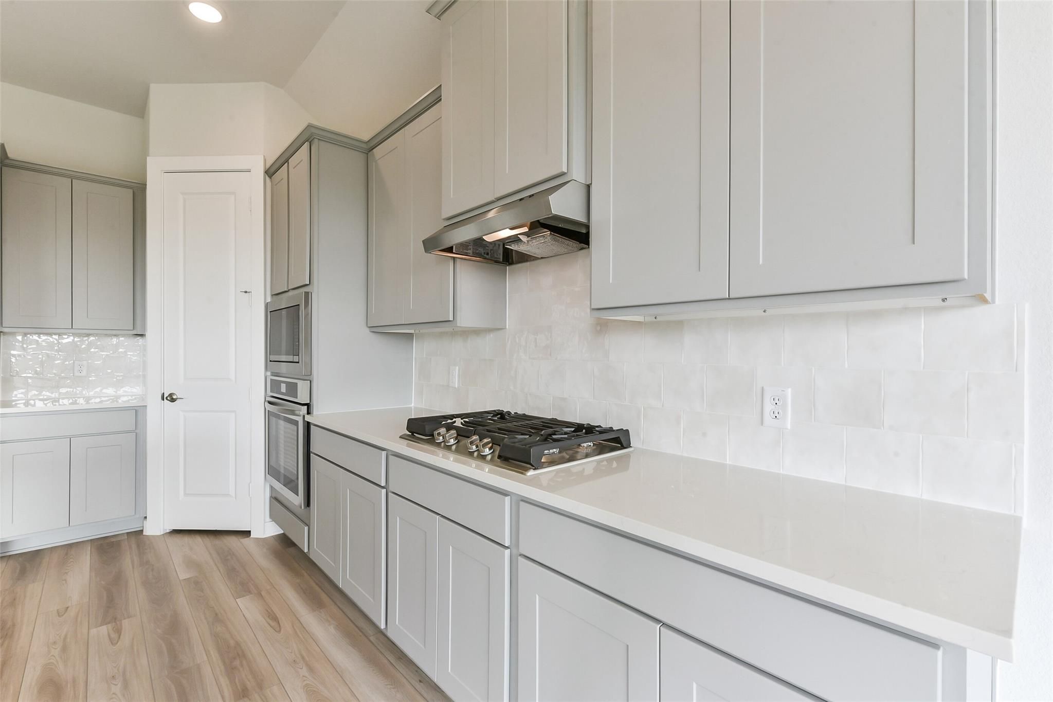 Modern white shaker kitchen with quartz counters, gas range, subway tile backsplash in Davidson Homes The Edward A, Lago Mar