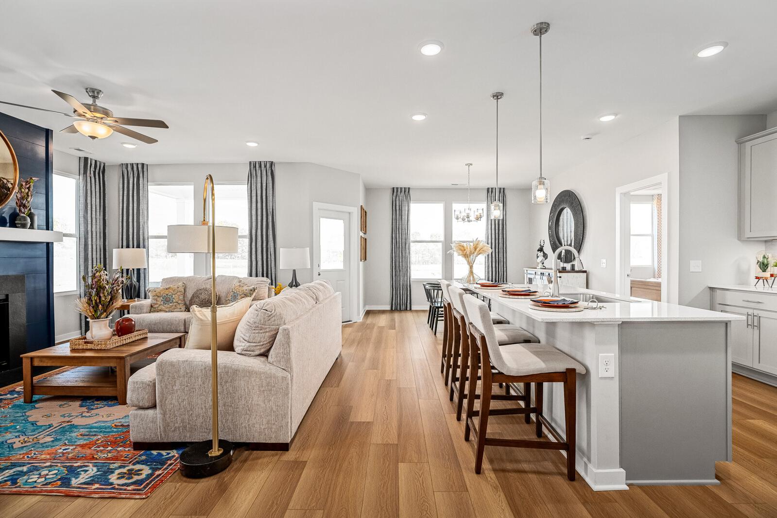 Open-concept living room and kitchen at Sage Farms in White House TN with hardwood floors, white island bar, and beige sofa seating