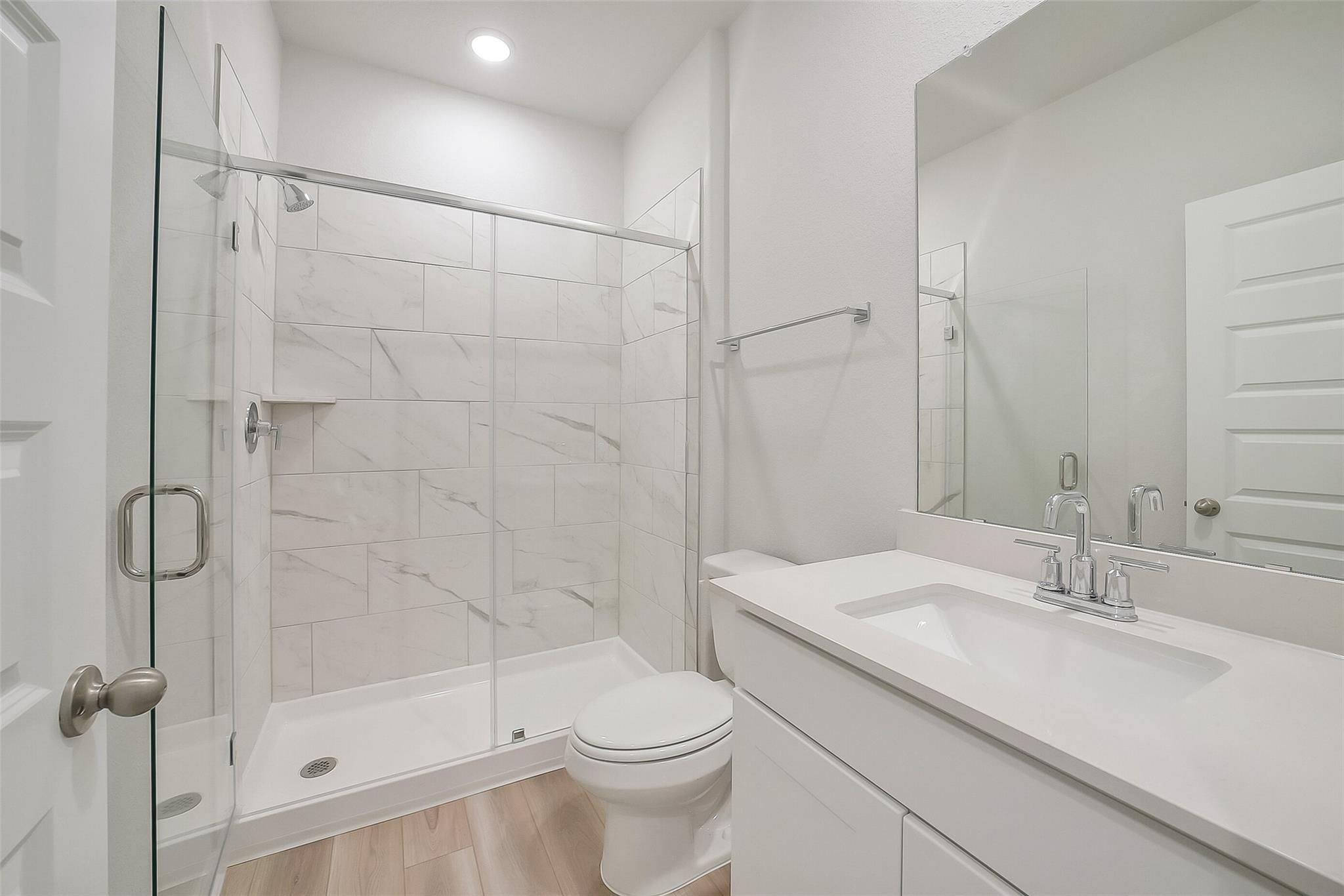 Modern white marble-look tiled walk-in shower with glass door in Davidson Homes The Acadia A bathroom, Sunterra, Katy, Texas