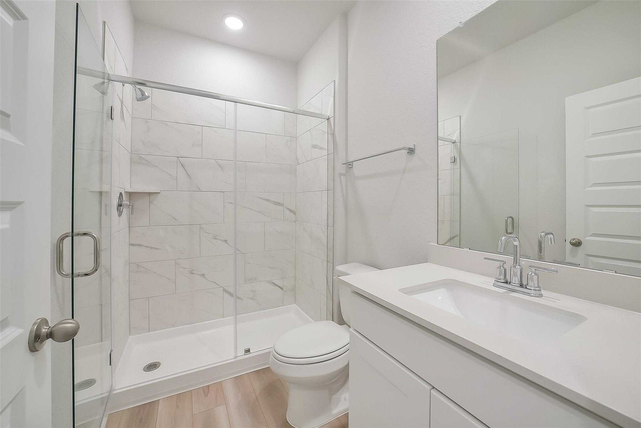 Modern white marble-look tiled walk-in shower with glass door in Davidson Homes The Acadia A bathroom, Sunterra, Katy, Texas